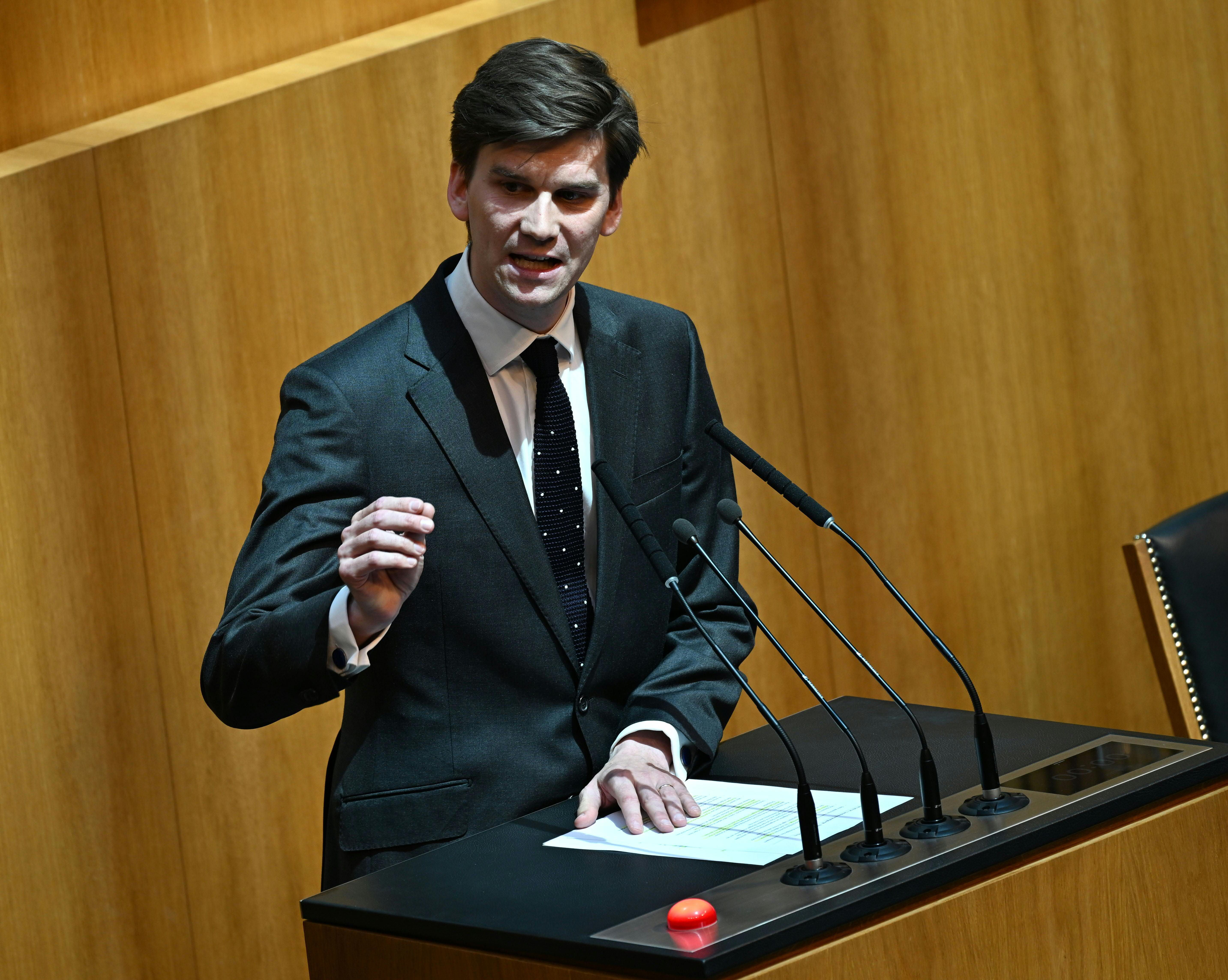 Ein Mann im Anzug spricht bei einer Rede an einem Pult mit mehreren Mikrofonen.
