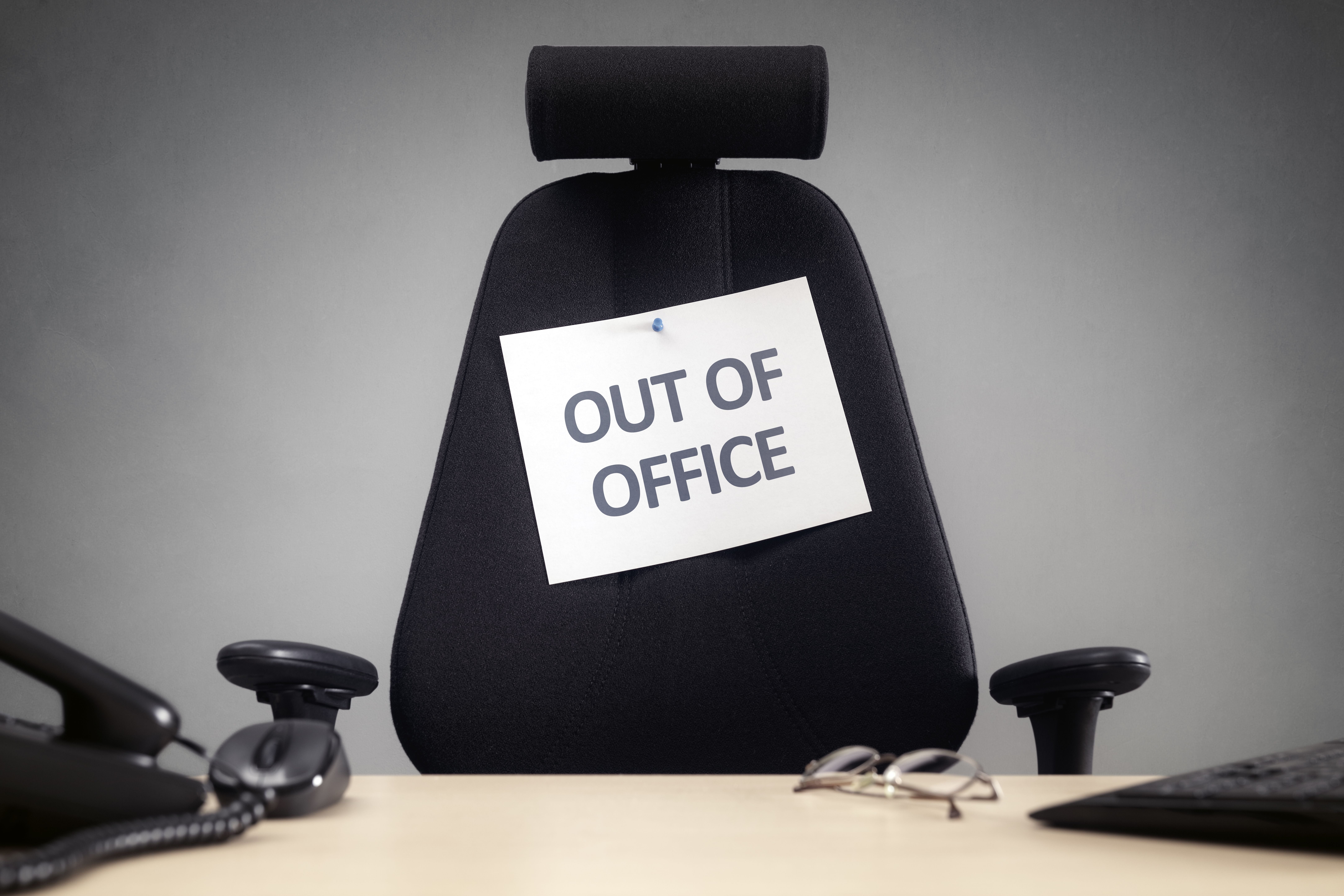 Bürostuhl mit Schild „Out of Office“ im leeren Büro vor Schreibtisch und Telefon.