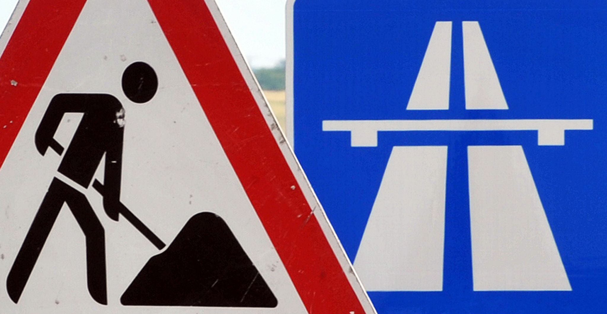 Ein Baustellenschild steht vor einem Autobahnschild.