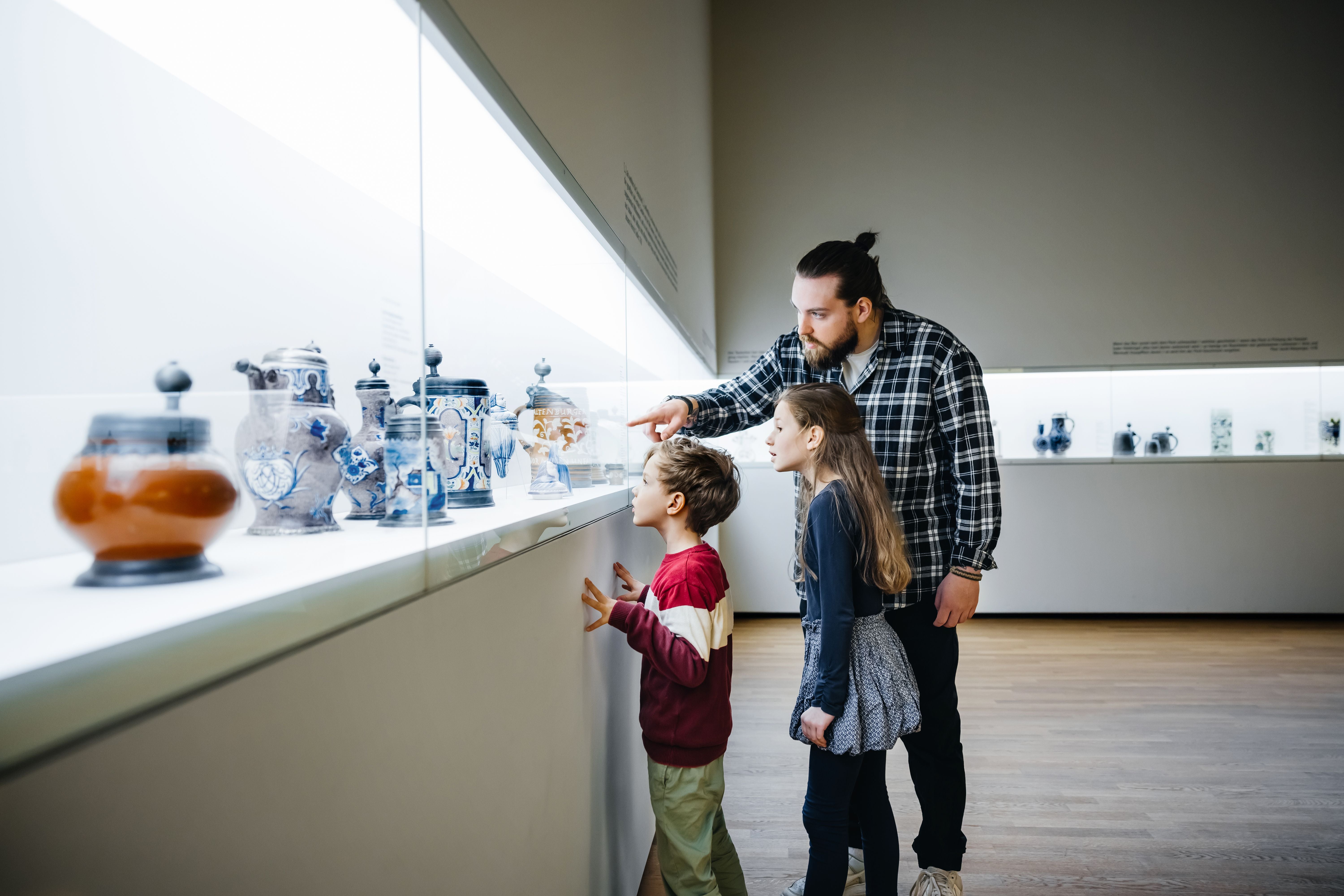Ein Vater zeigt seinen zwei Kindern Ausstellungsobjekte in einem Museum und erklärt sie ihnen.