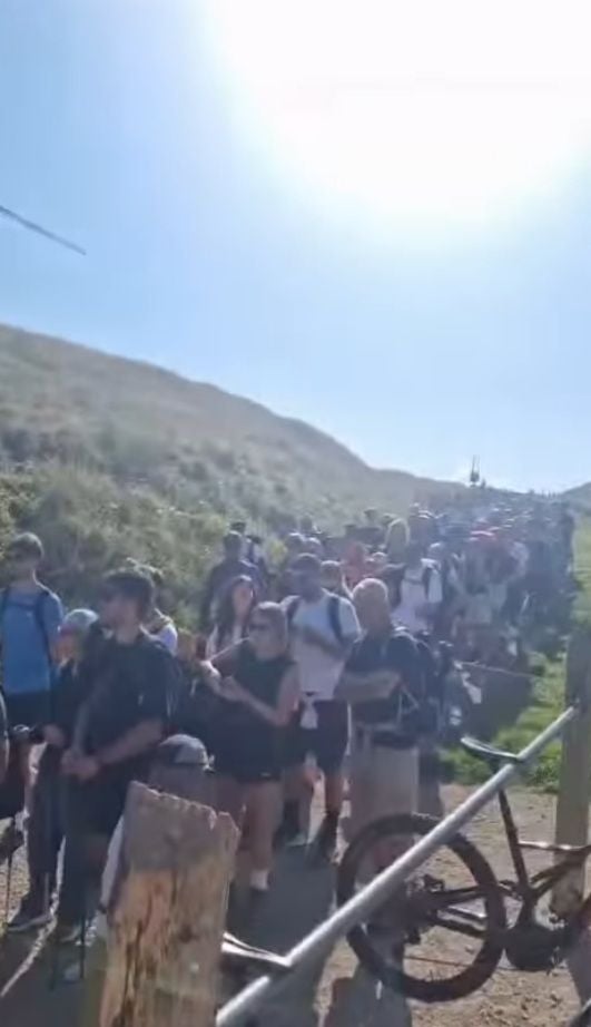 Viele Wanderer stehen bei Sonnenschein in einer langen Schlange auf einem Bergweg in Italien.