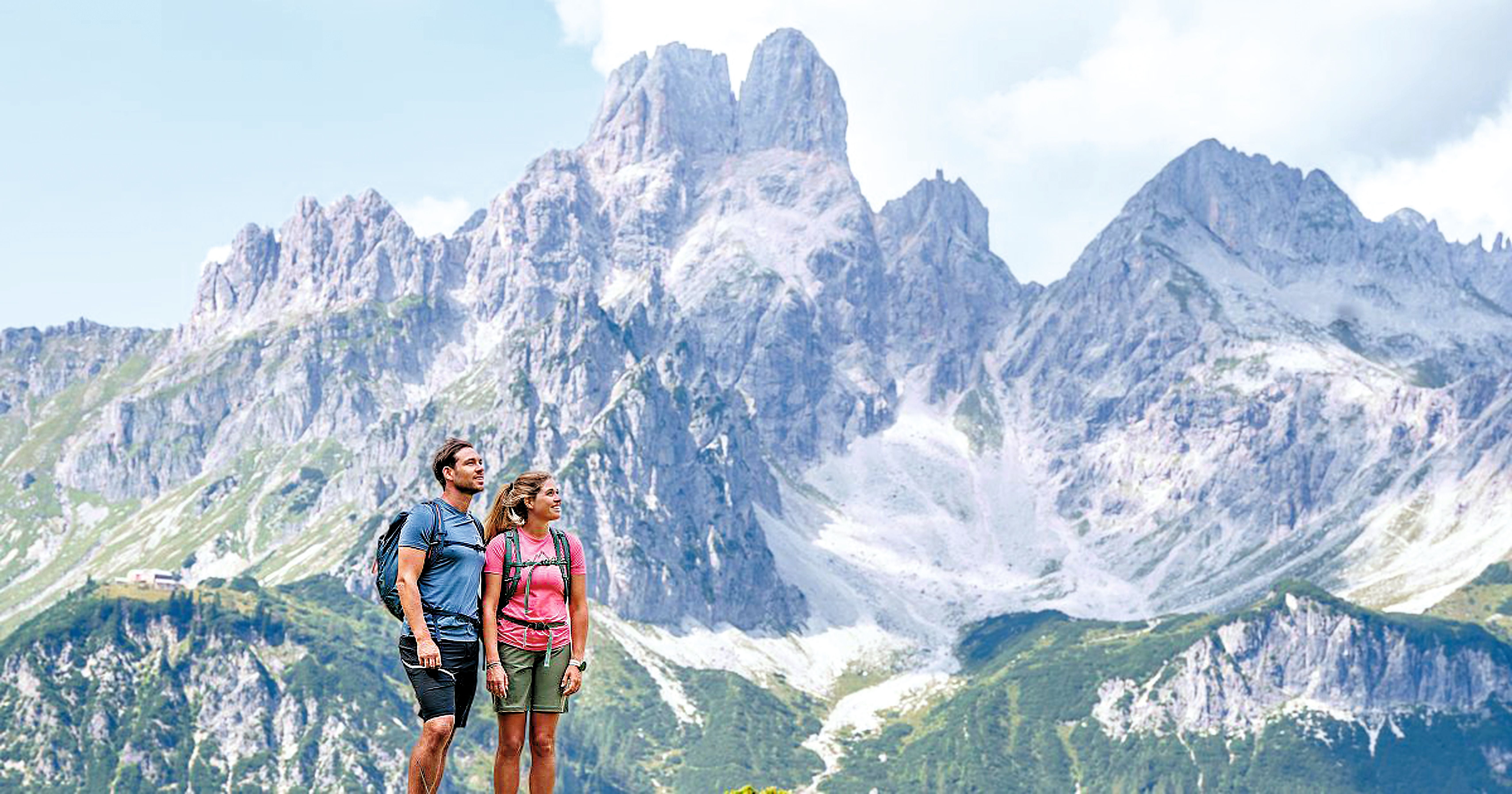 Zwei Wanderer stehen vor einer beeindruckenden Bergkulisse mit felsigen Gipfeln.