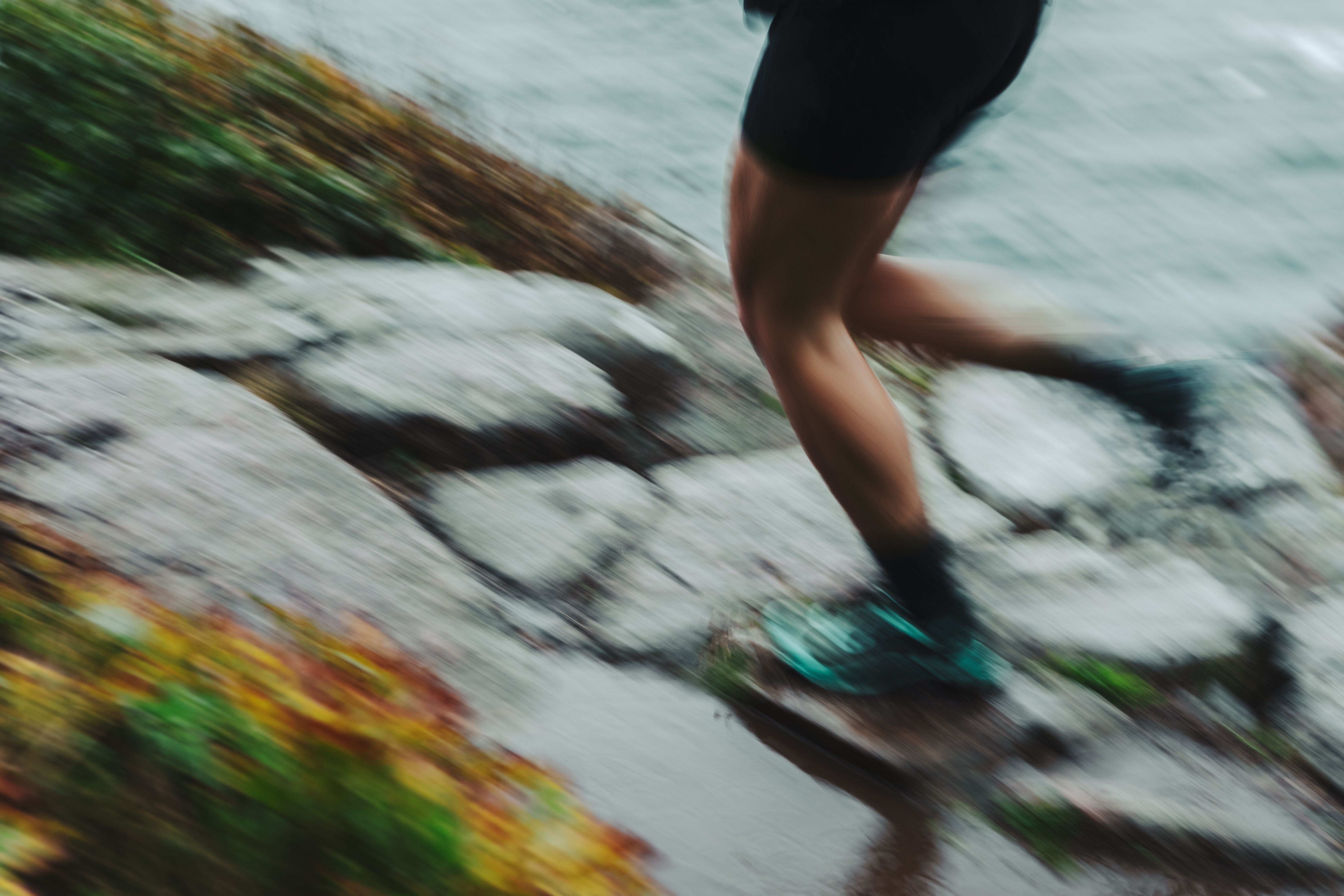 Verschwommene Nahaufnahme von Läuferbeinen auf einem steinigen, nassen Trail im Regen.