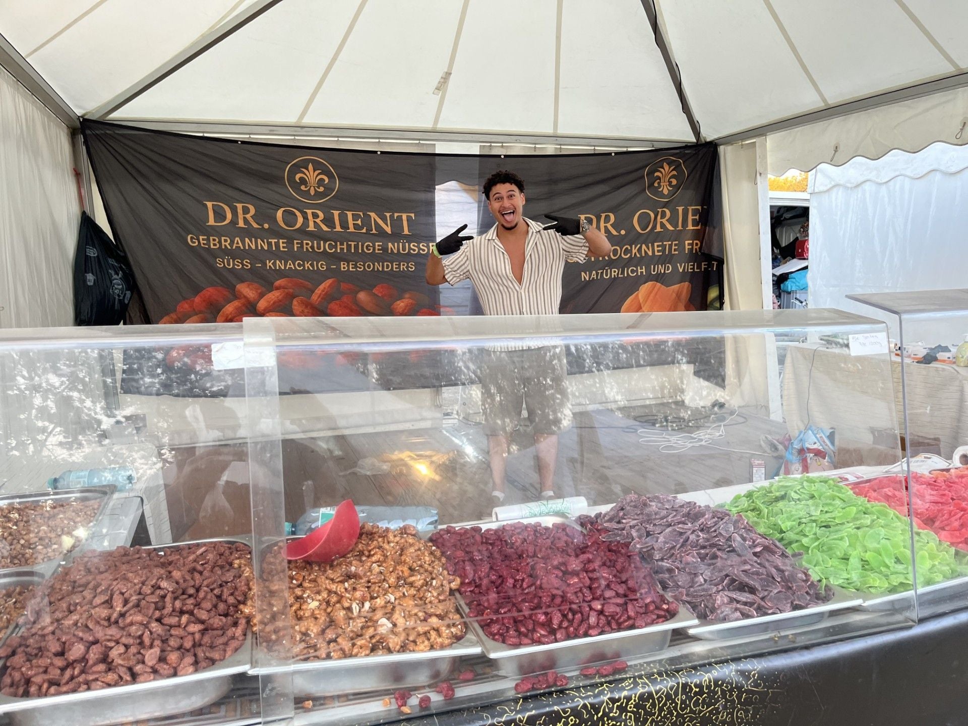 Mann steht fröhlich an einem Marktstand mit bunten Nüssen und Trockenfrüchten bei Afrika Tage.