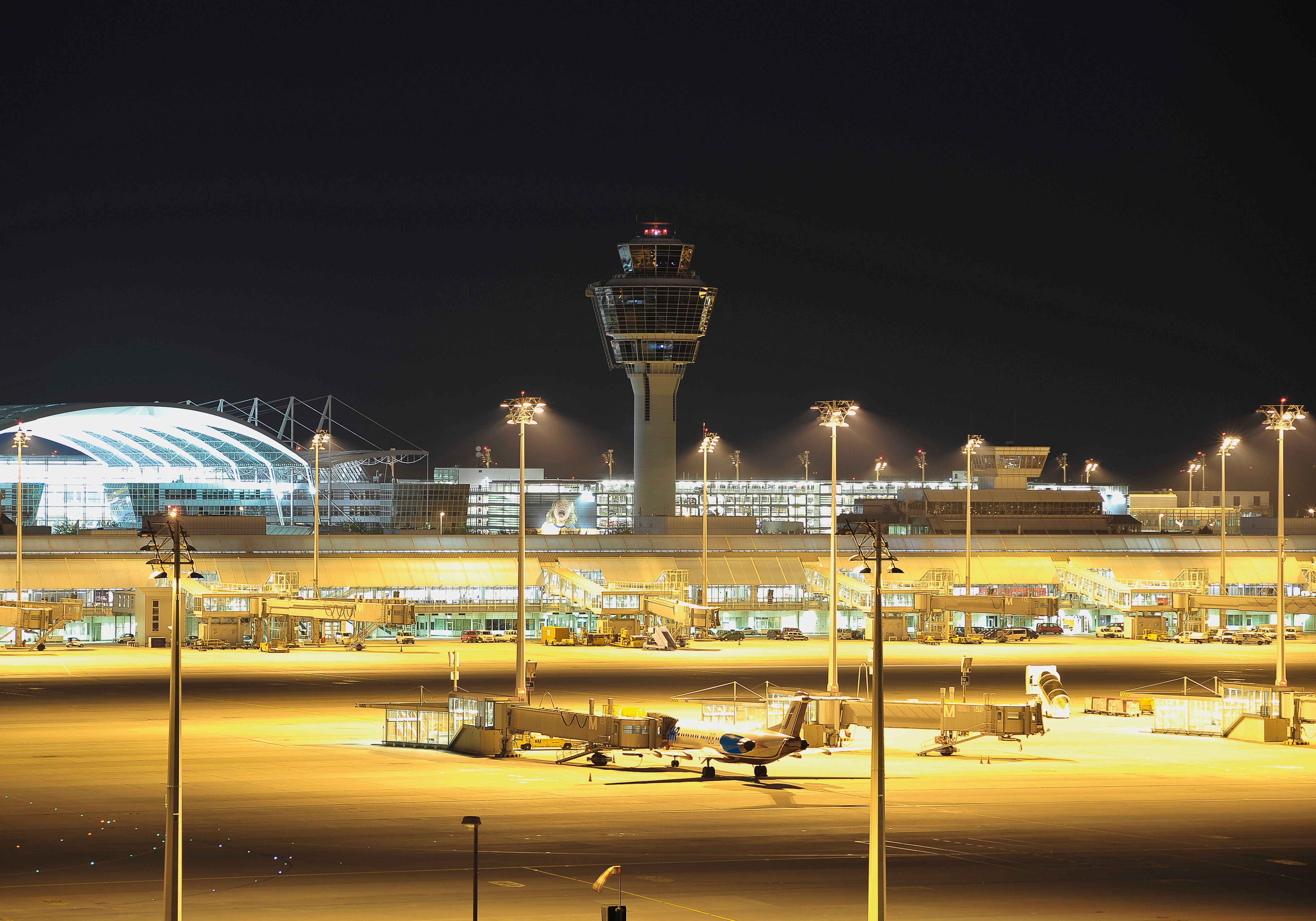 Nachtsicht auf den beleuchteten Flughafen München mit Tower und Terminals.