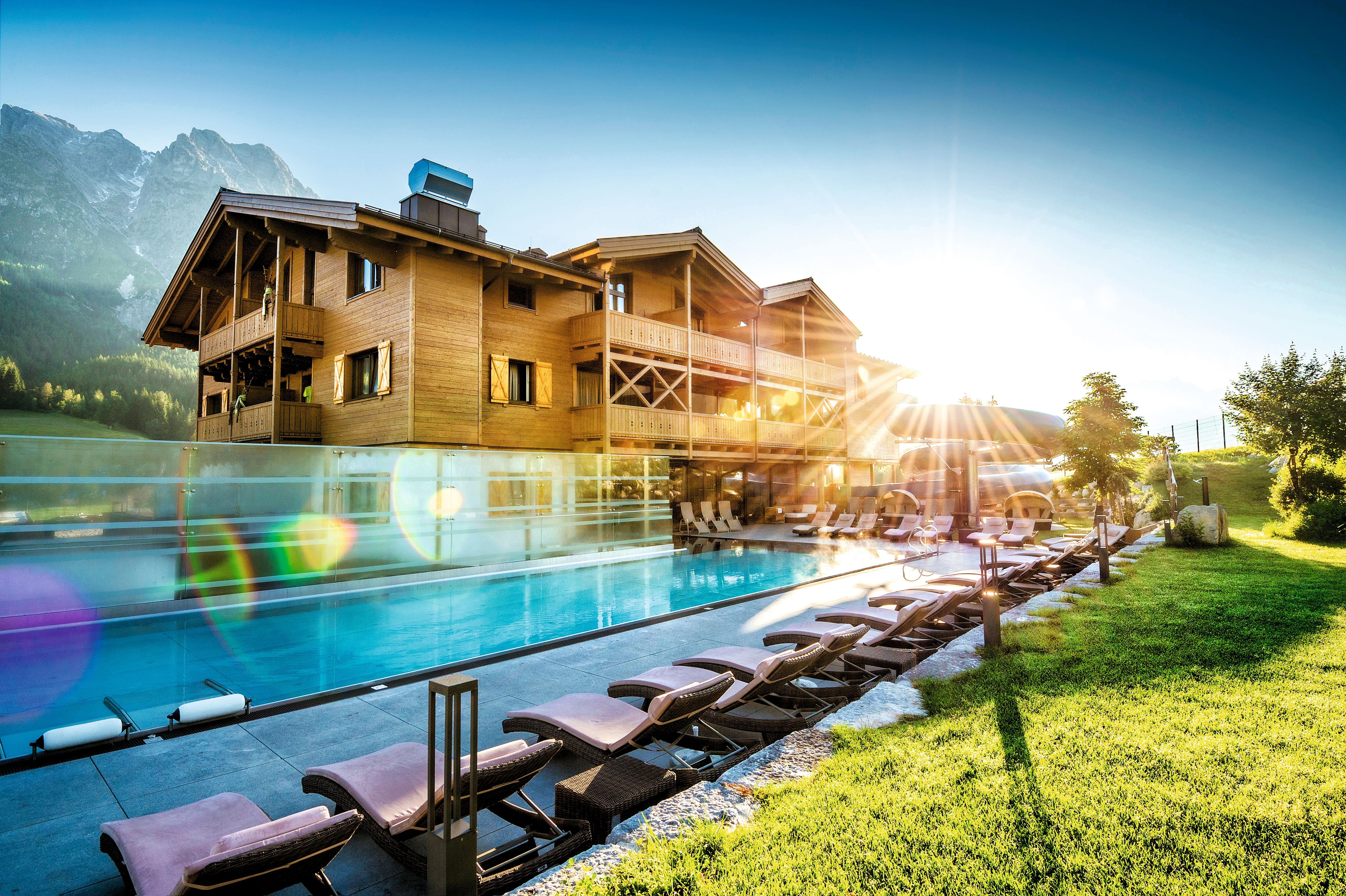 Holzgebäude mit Pool, Sonnenliegen und Berglandschaft bei Sonnenuntergang.