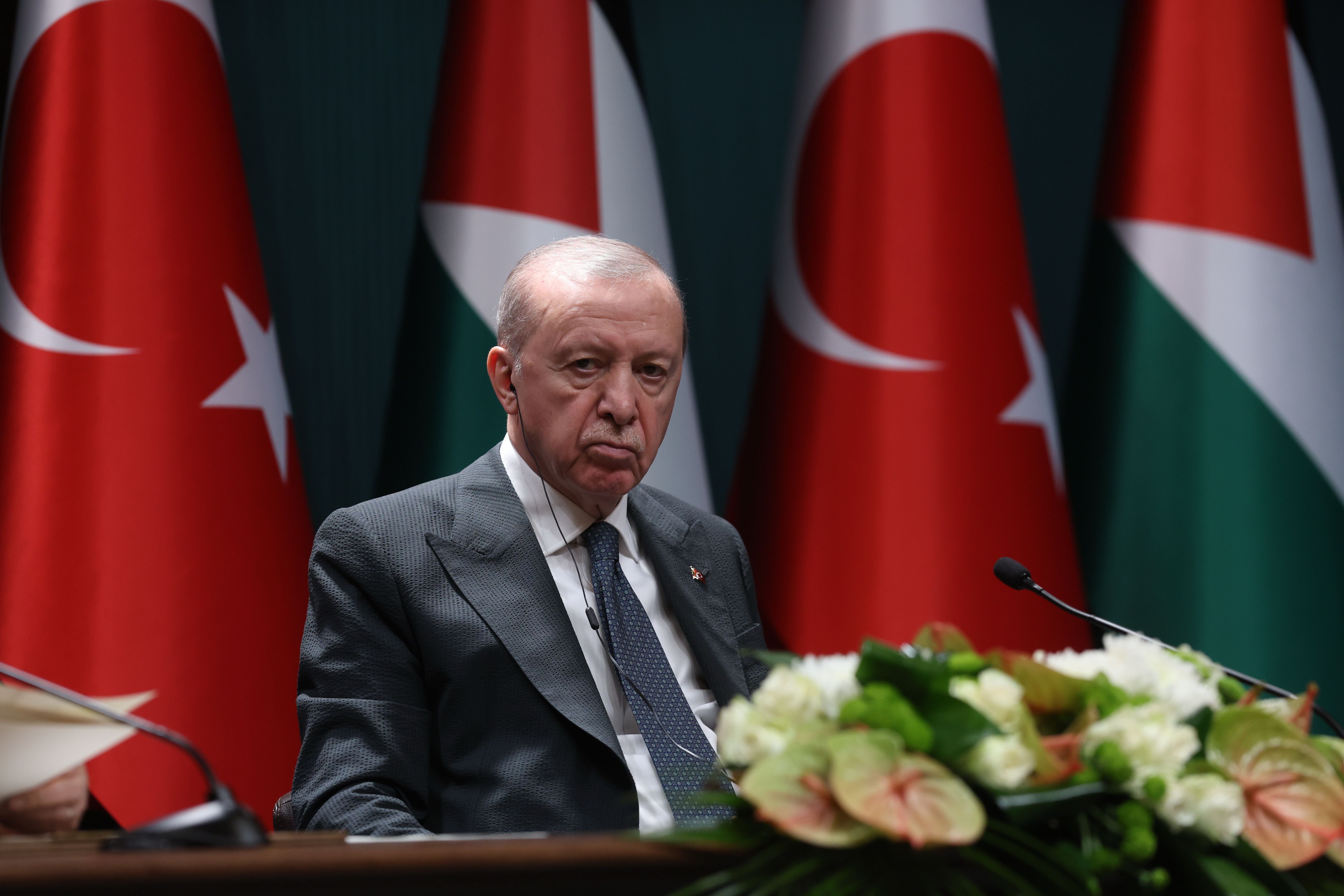 Ein Mann im Anzug sitzt vor Mikrofonen und türkischen sowie palästinensischen Flaggen.
