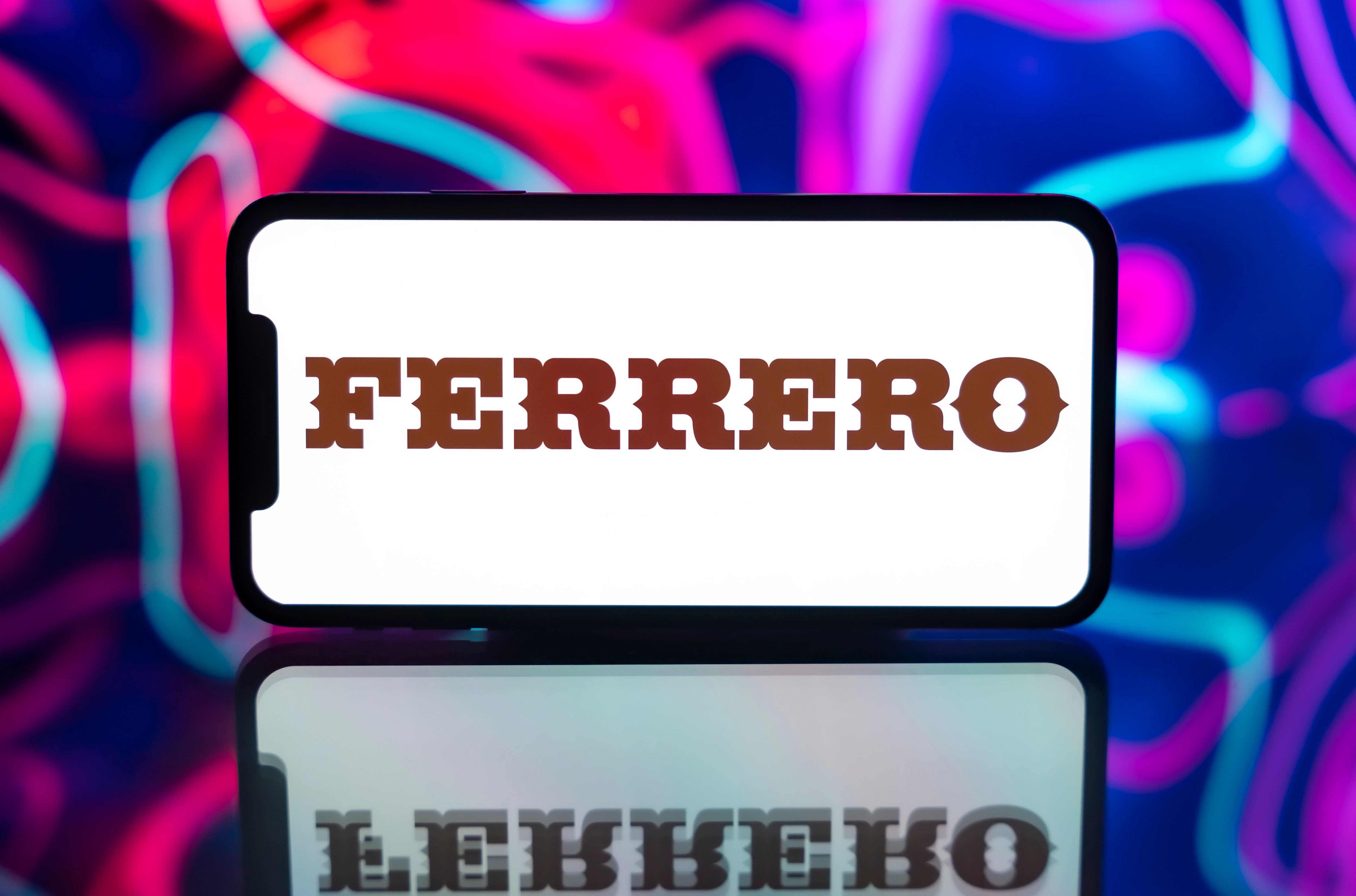 Das Ferrero-Logo wird auf einem Smartphone vor buntem Hintergrund angezeigt.