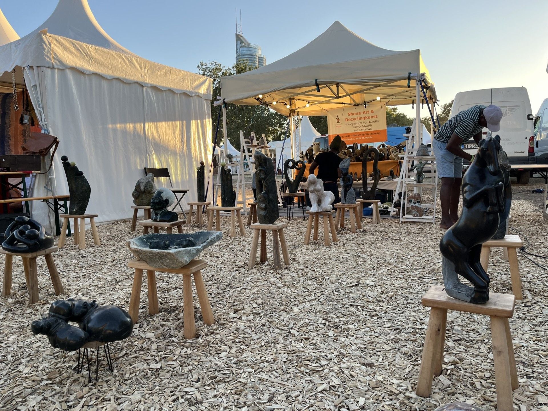 Kunsthandwerksmarkt mit afrikanischen Steinskulpturen auf Hockern unter Zelten bei Afrika Tage.