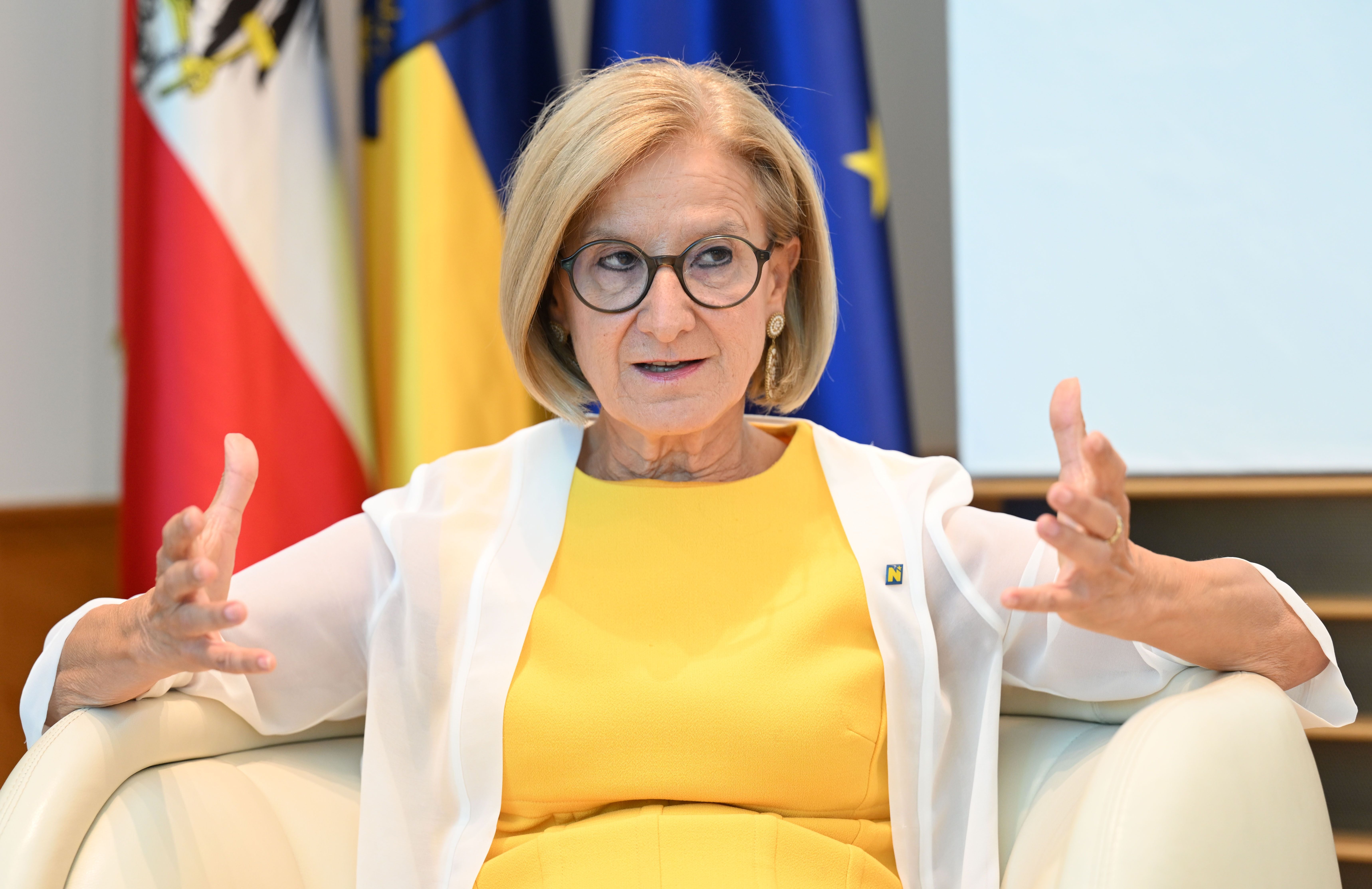 Eine Frau im gelben Kleid spricht gestikulierend in einem Interview vor Fahnen im Hintergrund.