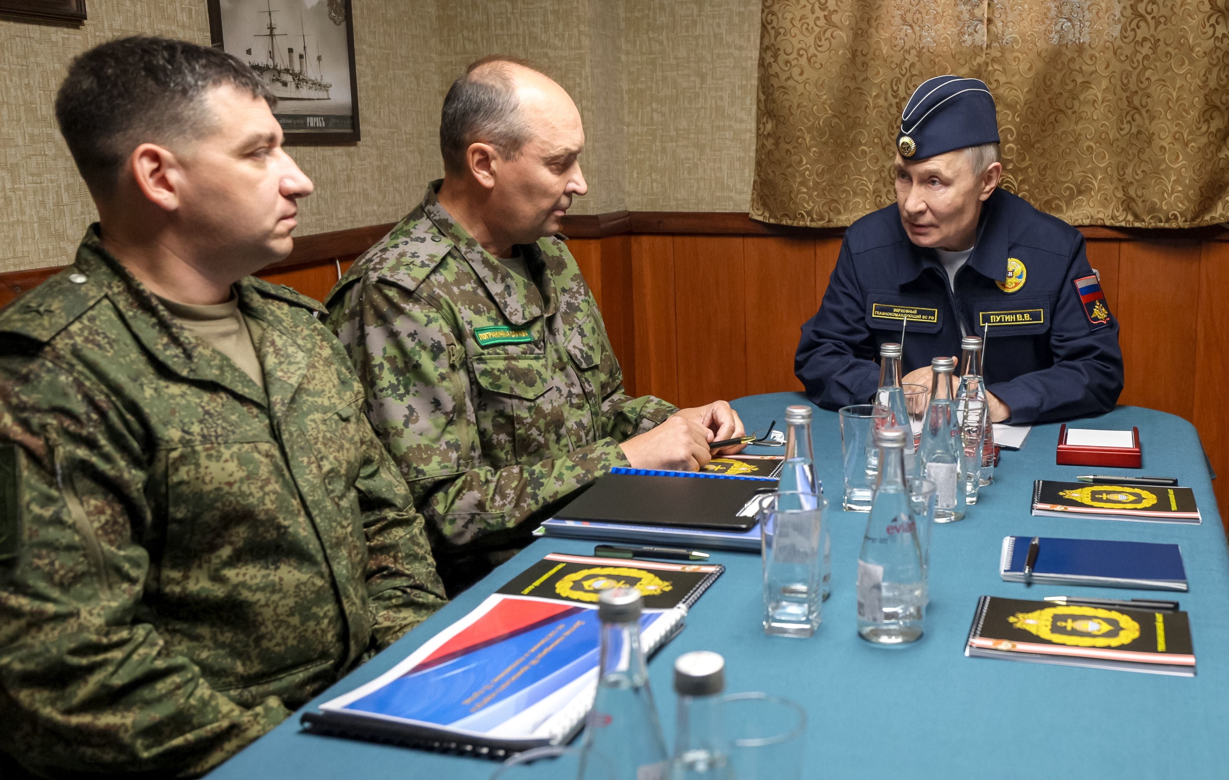 Drei Männer in Militäruniformen sitzen an einem Tisch mit Wasserflaschen und Notizbüchern.