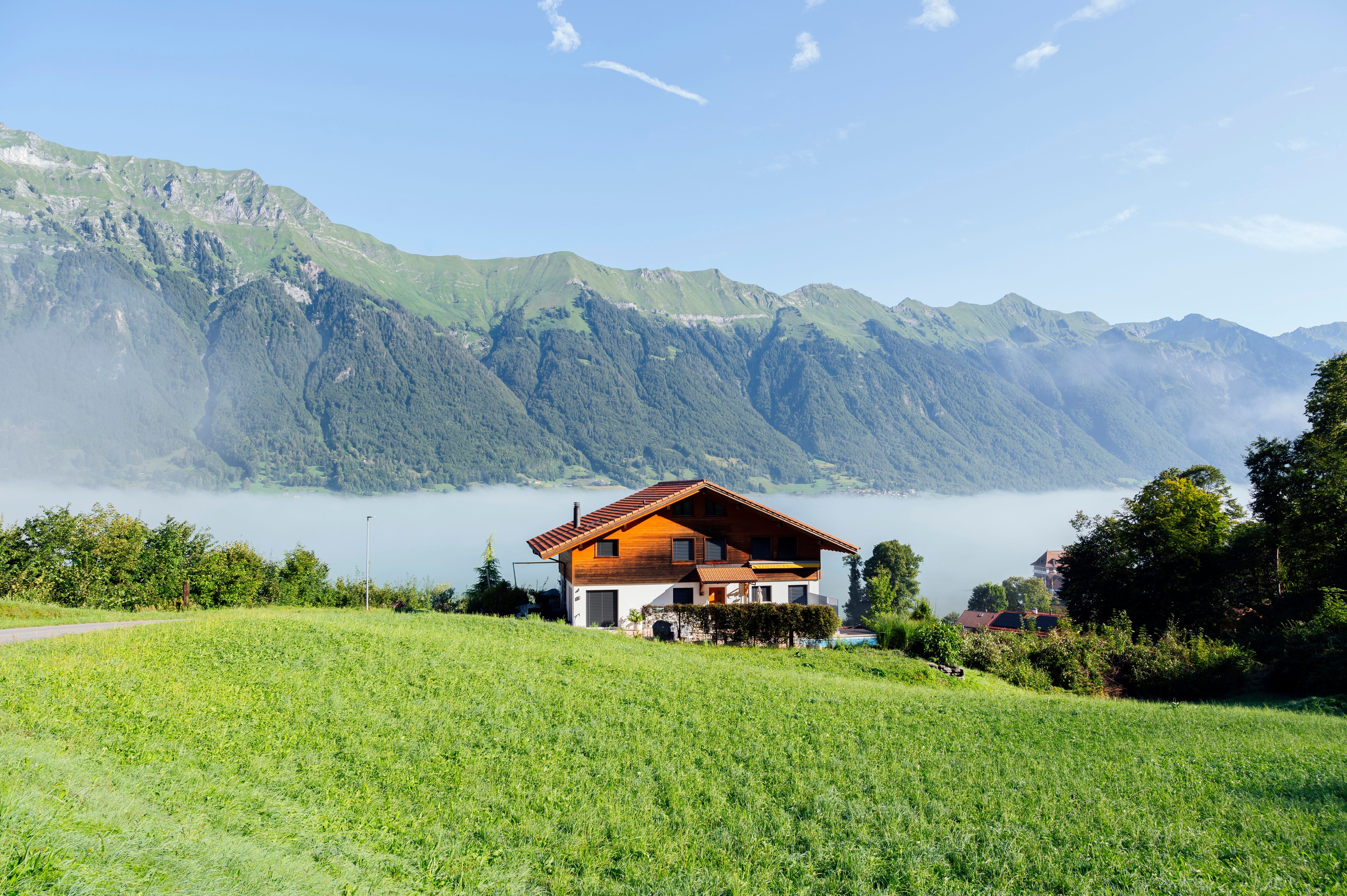 Haus in der Schweiz vor grünen Bergen und über einem nebligen Tal, bei klarem Himmel.