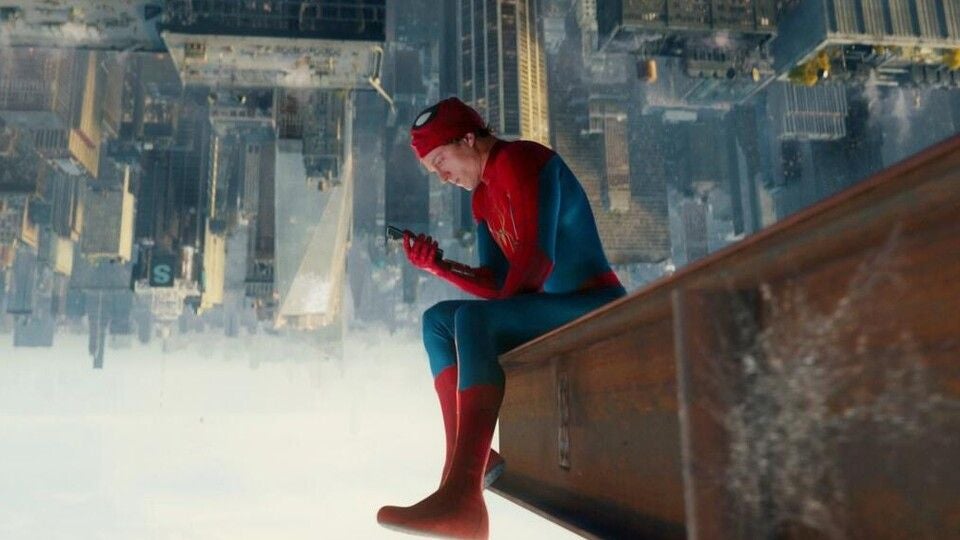 Spider-Man sitzt an einem Hochhaus und schaut auf sein Handy, die Stadt ist kopfüber im Hintergrund.