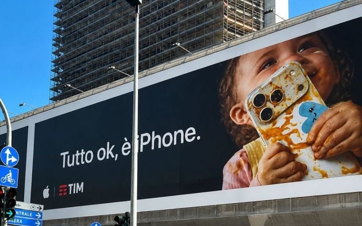 Werbeplakat mit Kind, das ein schmutziges iPhone hält und lächelt, Text: „Tutto ok, è iPhone.“