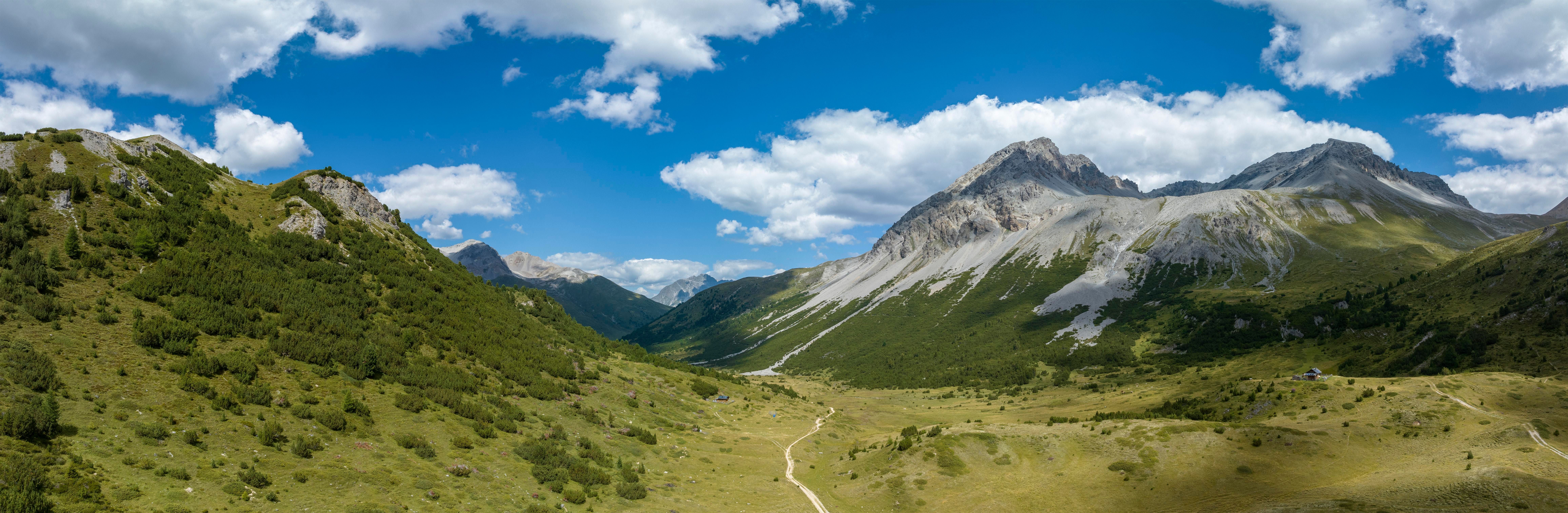 Weitläufiges Tal in Südtirol mit grünen Wiesen, Wanderweg und hohen Bergen unter blauem Himmel.