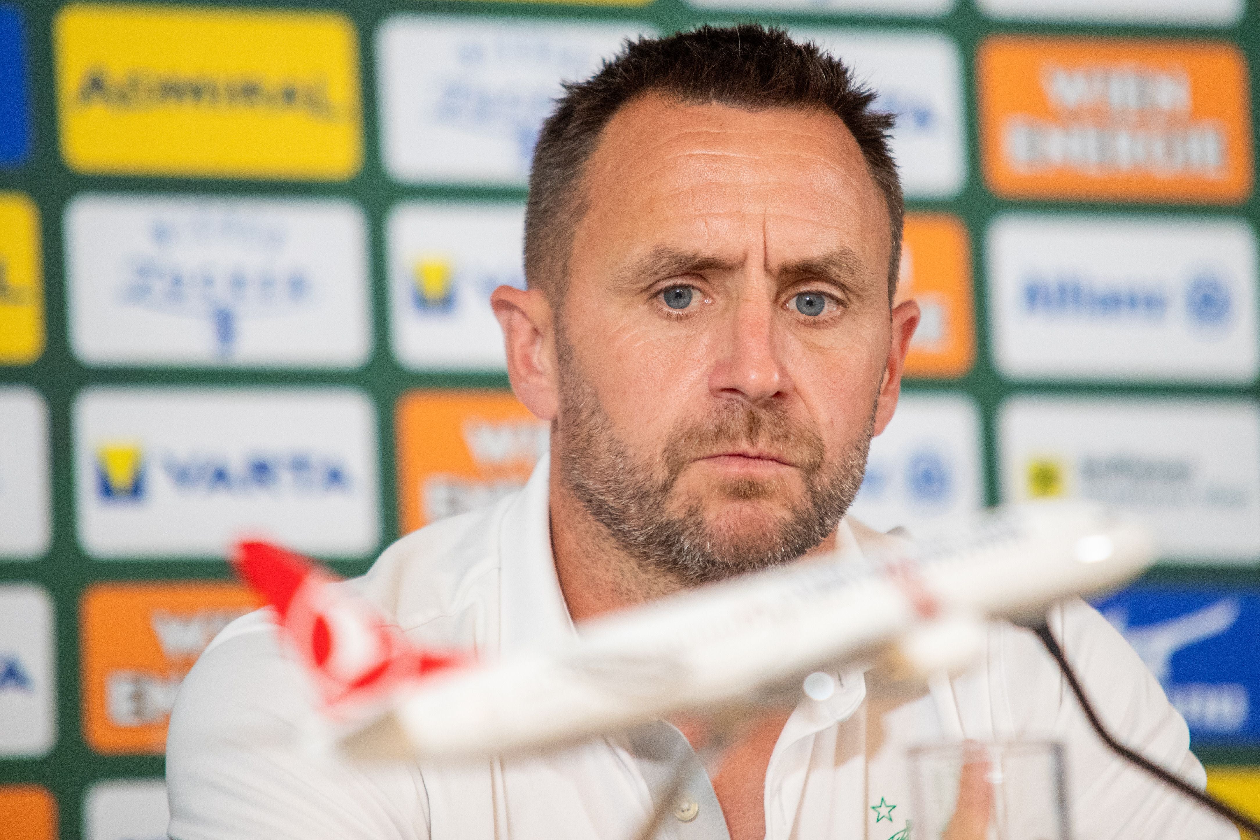 Ein Mann bei einer Pressekonferenz sitzt vor einer Modellflugzeug und Werbetafeln im Hintergrund.