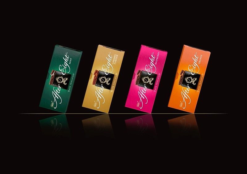 Vier Packungen After Eight Pralinen in verschiedenen Geschmacksrichtungen auf schwarzem Hintergrund.