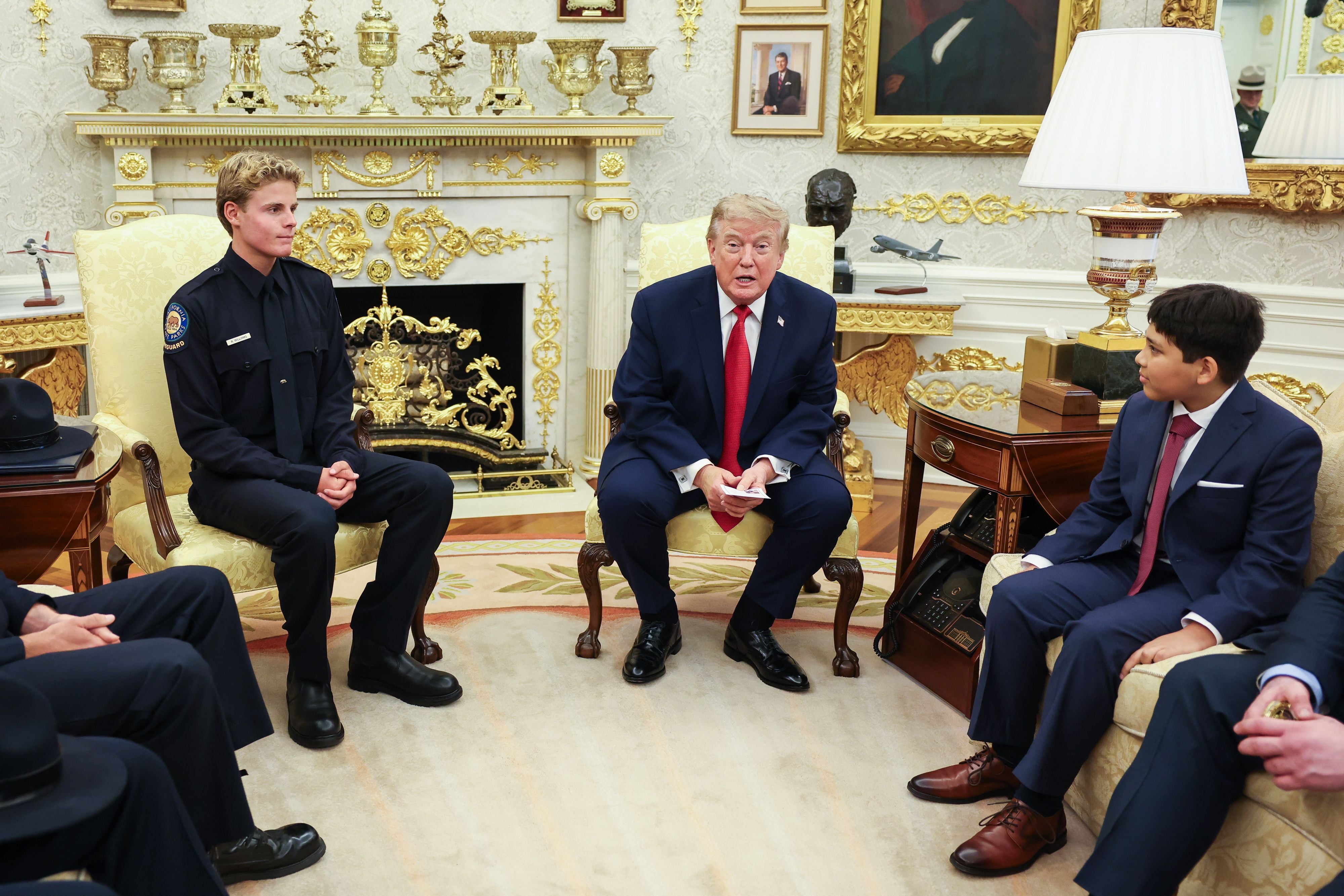 Drei Personen im Anzug und eine Person in Uniform sitzen im Oval Office und unterhalten sich.