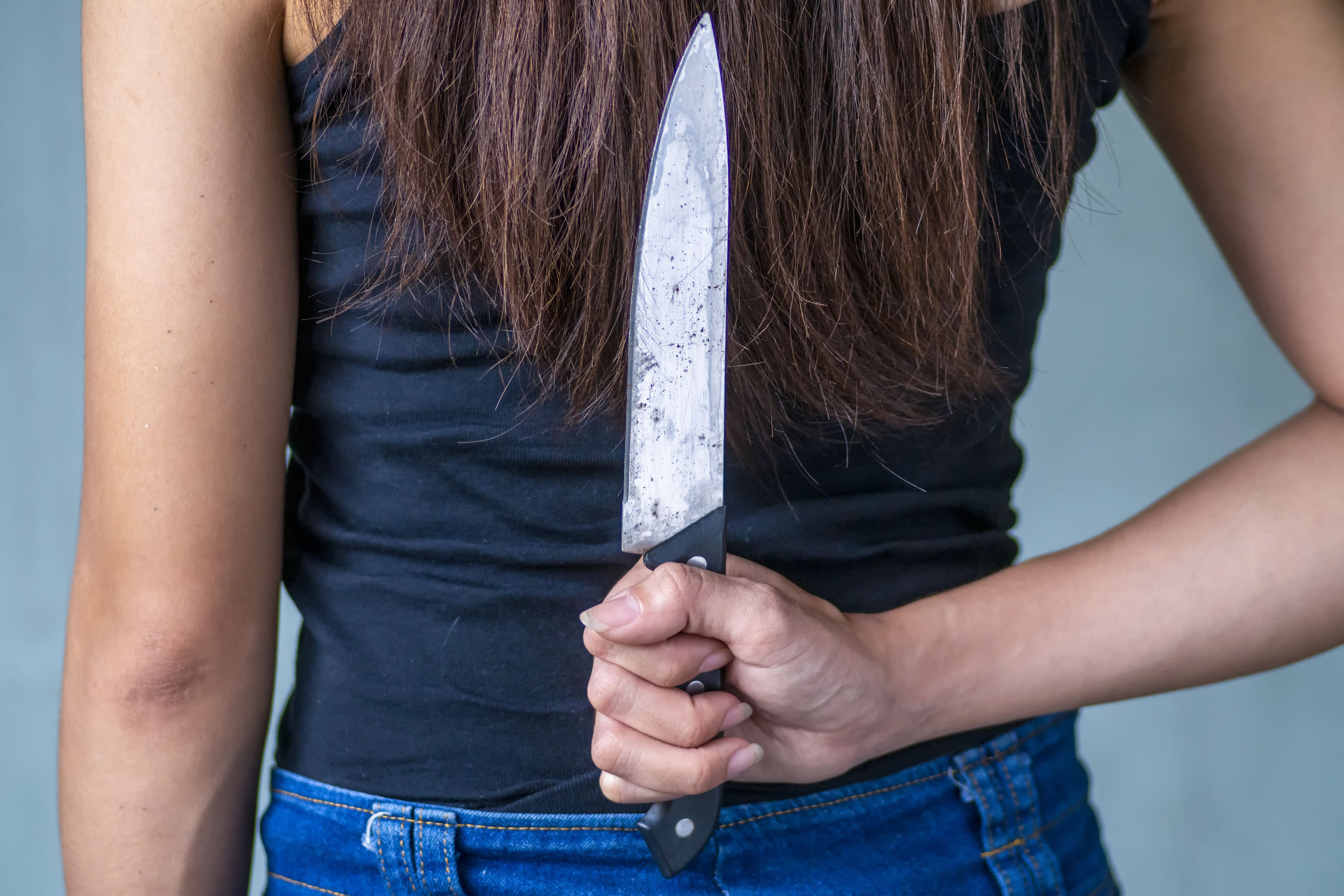 Frau hält ein großes Messer hinter ihrem Rücken versteckt.