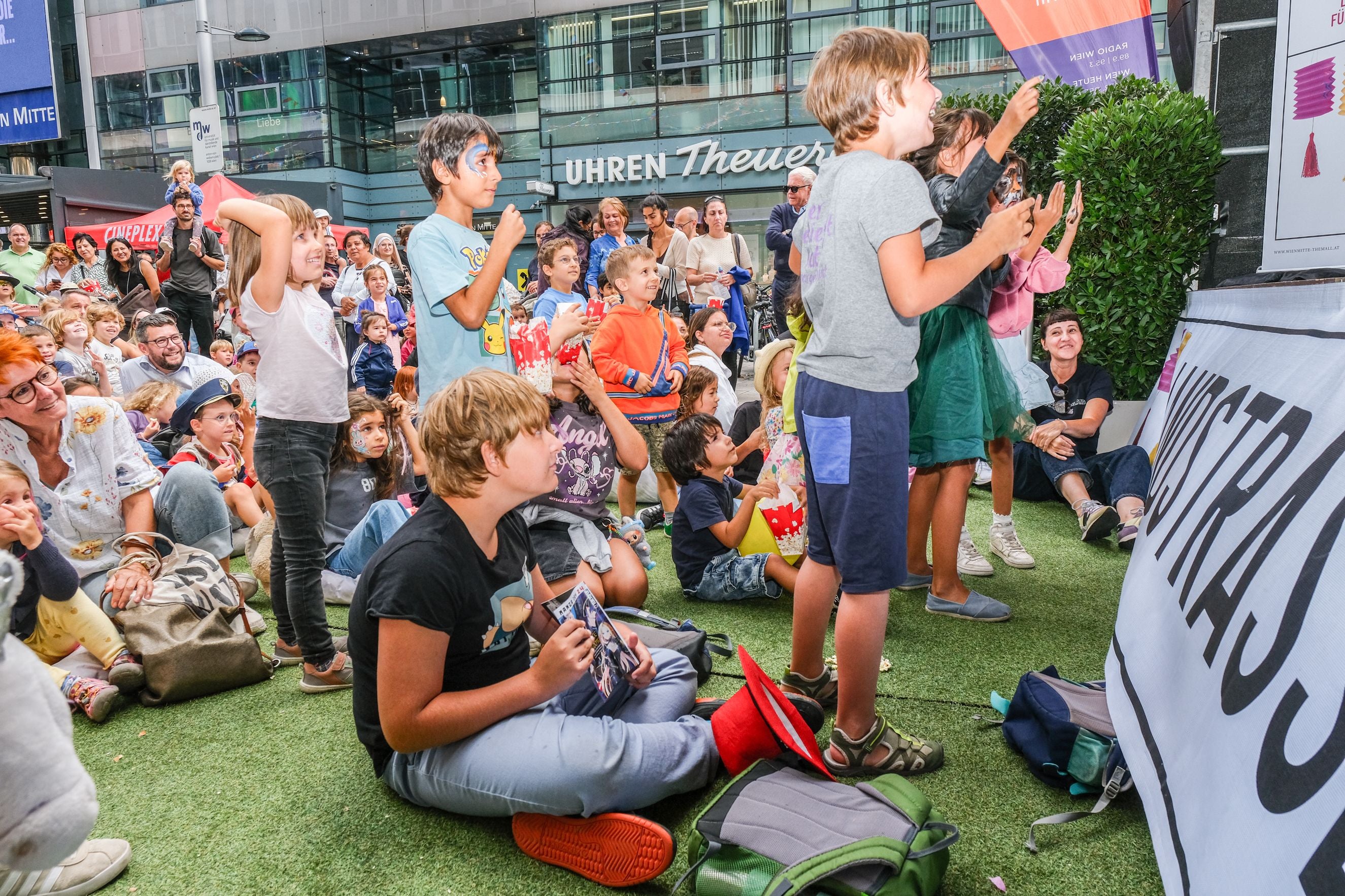 Viele Kinder sitzen und stehen lachend beim Landstraßenfest vor einer Bühne im Freien.