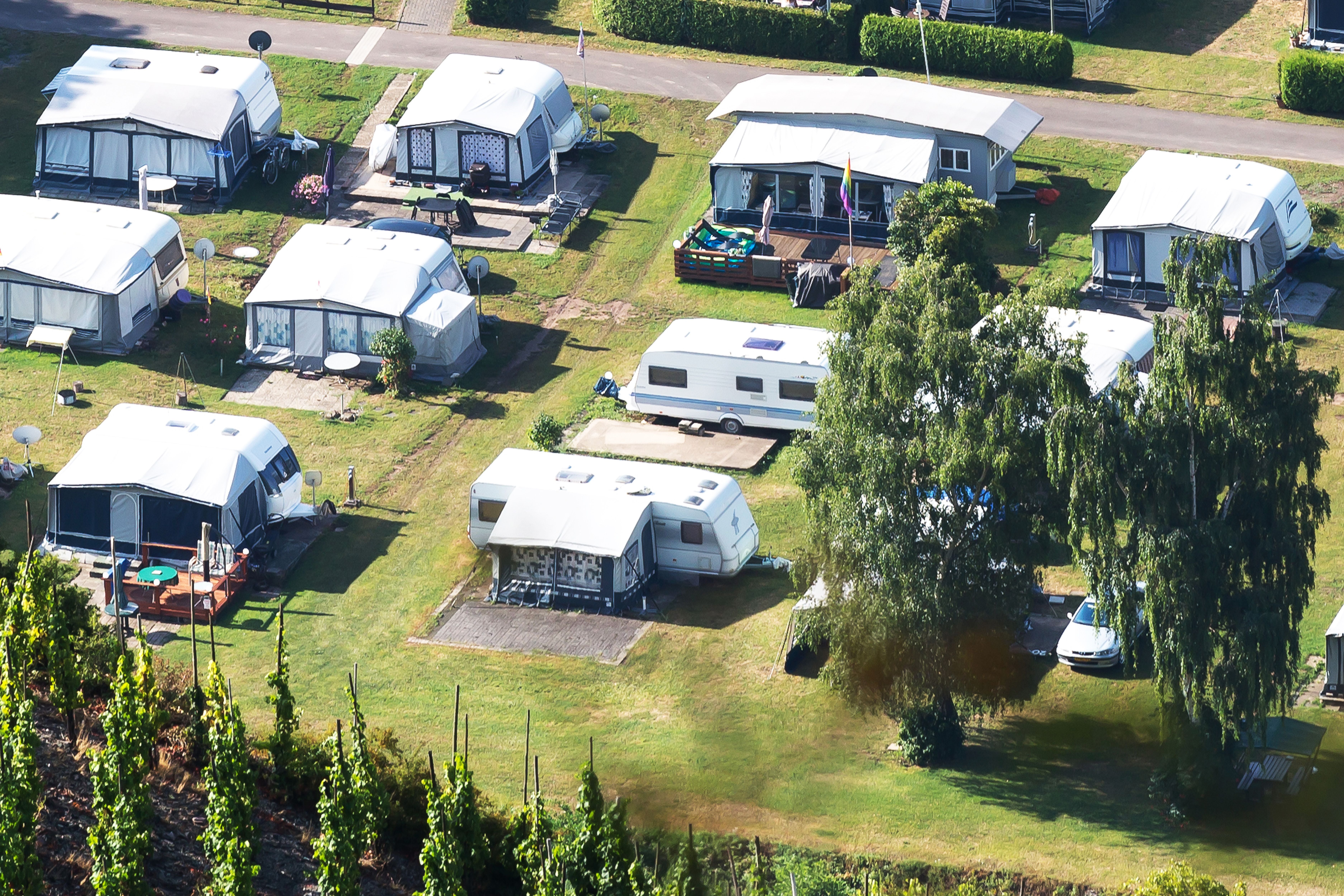 Mehrere Dauercampingplätze mit Wohnwagen und Vorzelten auf einer grünen Wiese nahe der Mosel.