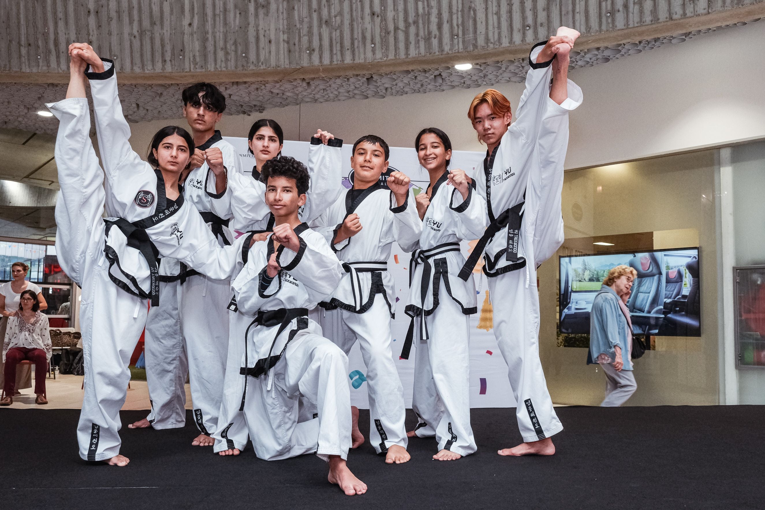 Sieben junge Taekwondo-Kämpfer posieren in Uniformen mit schwarzen Gürteln auf einer Bühne.