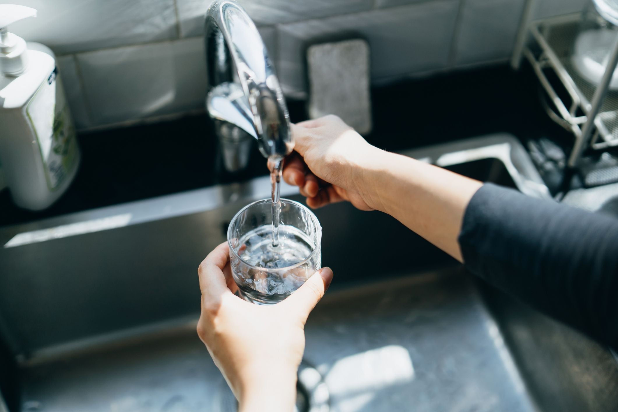 Frau füllt ein Glas mit Wasser aus dem Wasserhahn in der Küchenspüle.