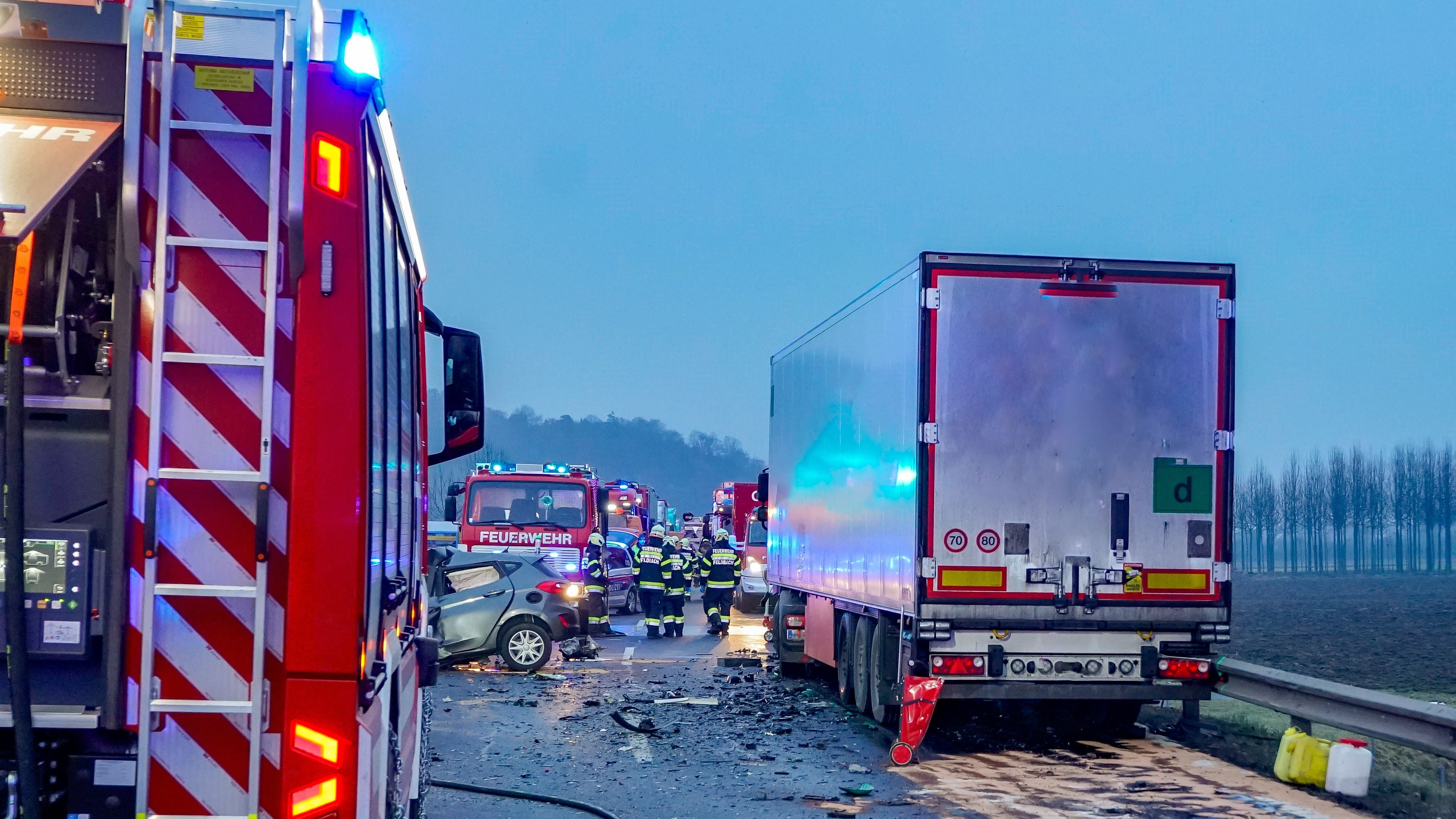 Unfallstelle mit Feuerwehr, beschädigtem Auto und Lkw auf einer Straße bei Dämmerung.