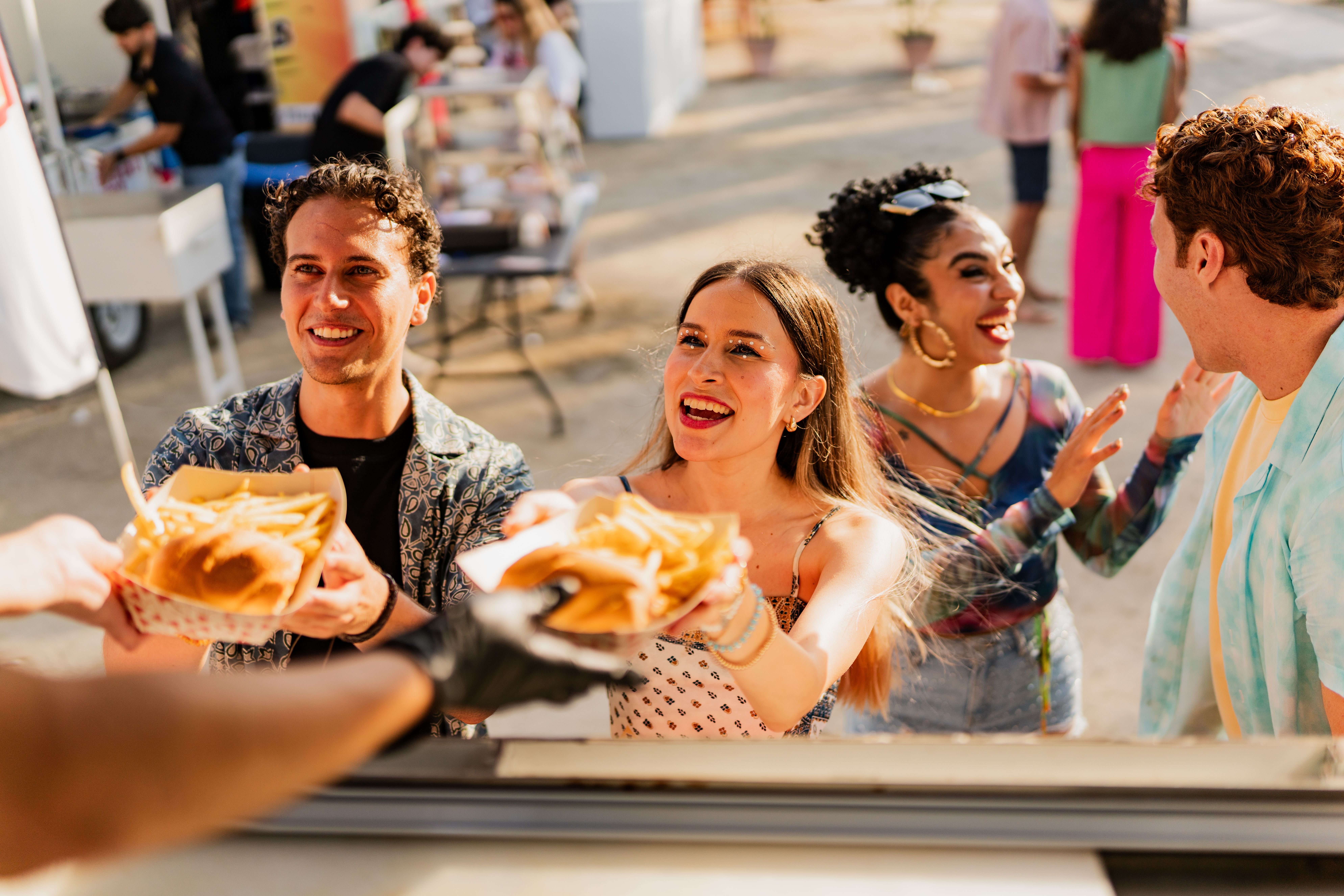 Junge Freunde holen sich draußen Essen an einem Foodtruck und lachen dabei.