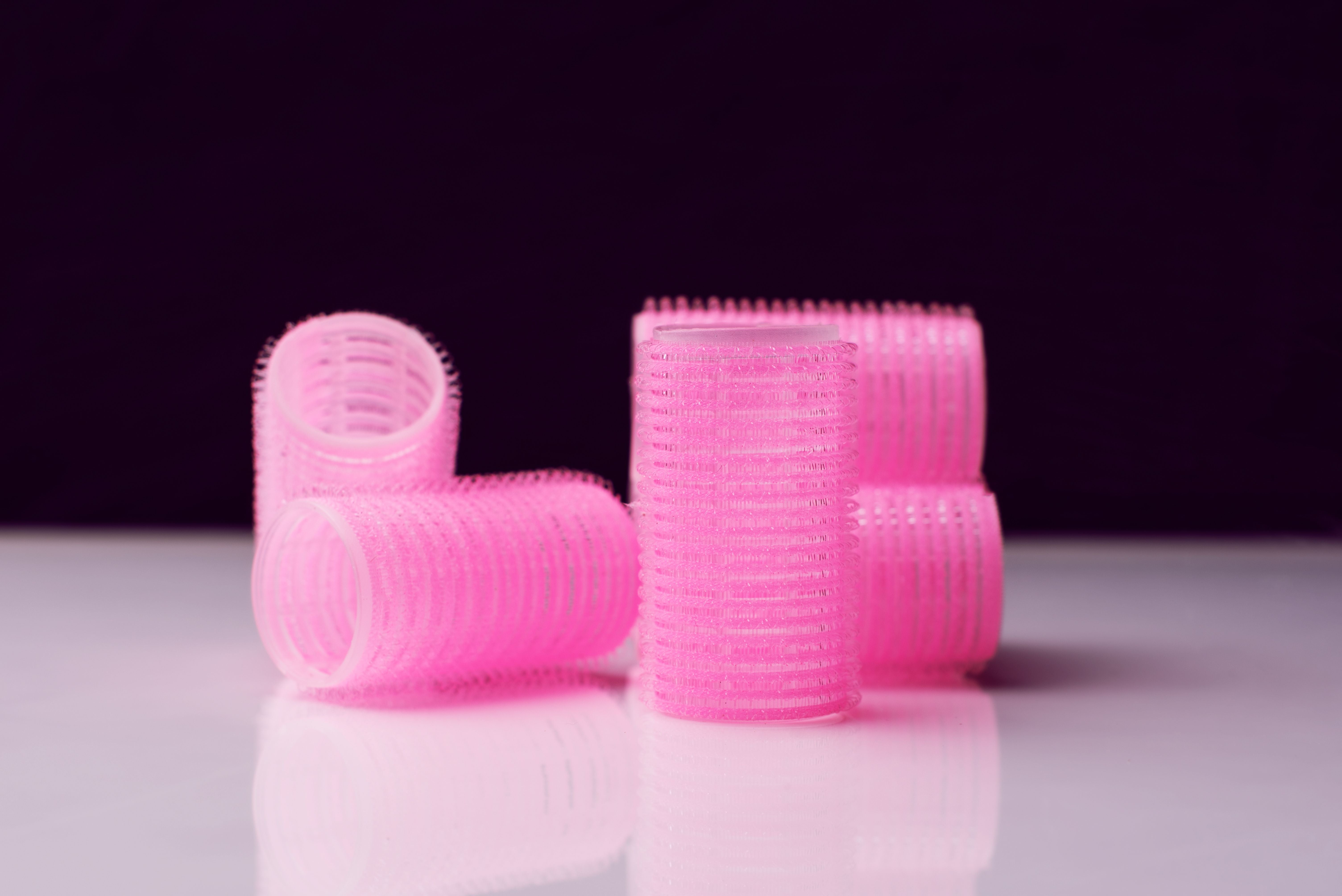 Fünf pinke Lockenwickler stehen auf einer glänzenden Oberfläche vor schwarzem Hintergrund.