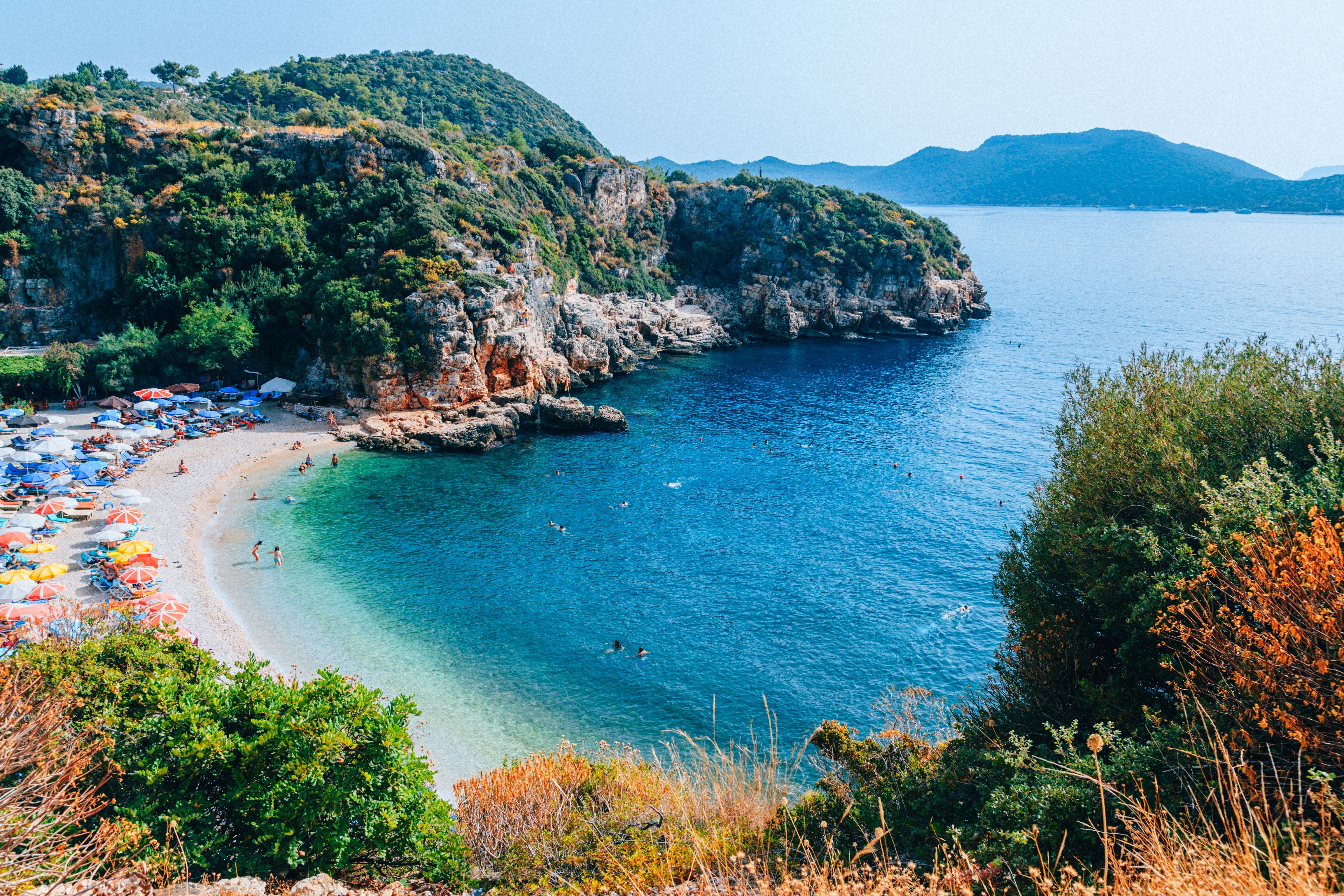 Blick auf die Bucht Büyük Çakil Plaji mit Strand, bunten Sonnenschirmen und klarem türkisblauem Wasser.