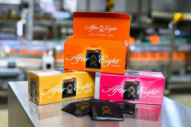 Drei bunte After Eight-Schachteln in verschiedenen Sorten auf einem Tisch, vorne Pralinen.