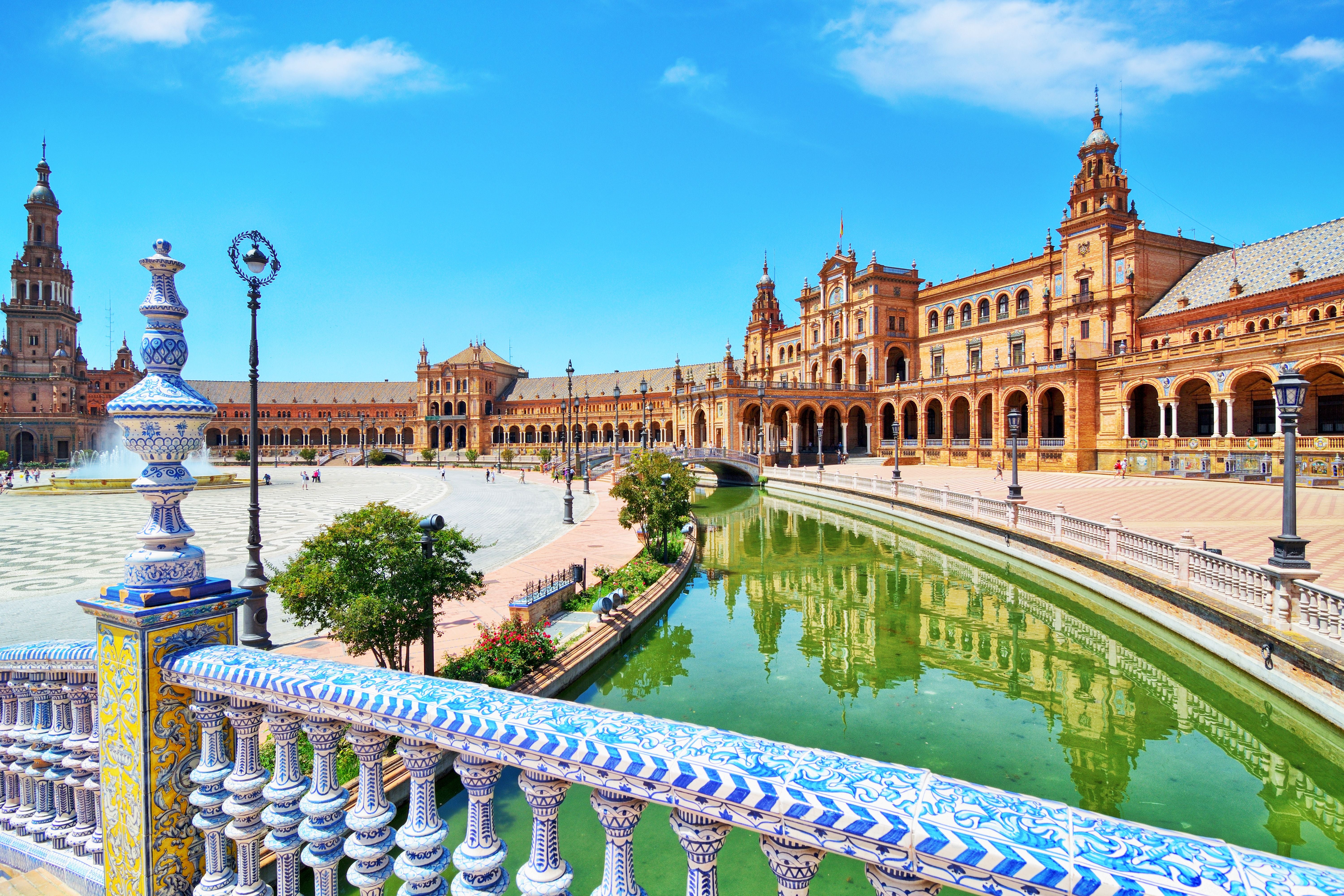Plaza de España in Sevilla mit Kanal, Springbrunnen und reich verzierten Brüstungen an einem sonnigen Tag.