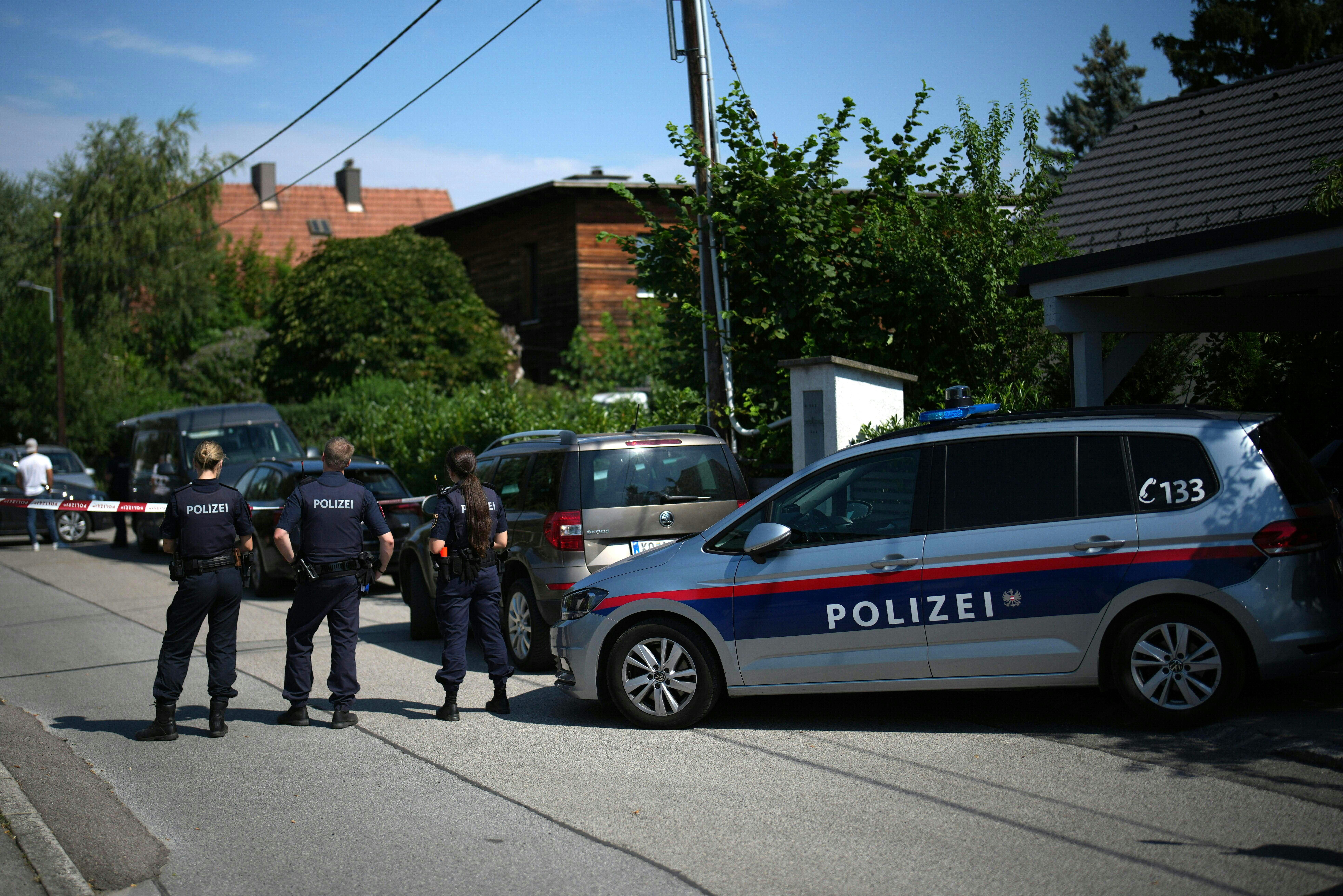 Drei Polizisten und ein Polizeiauto stehen in einer Wohnsiedlung nahe einem Tatort in Langenzersdorf.