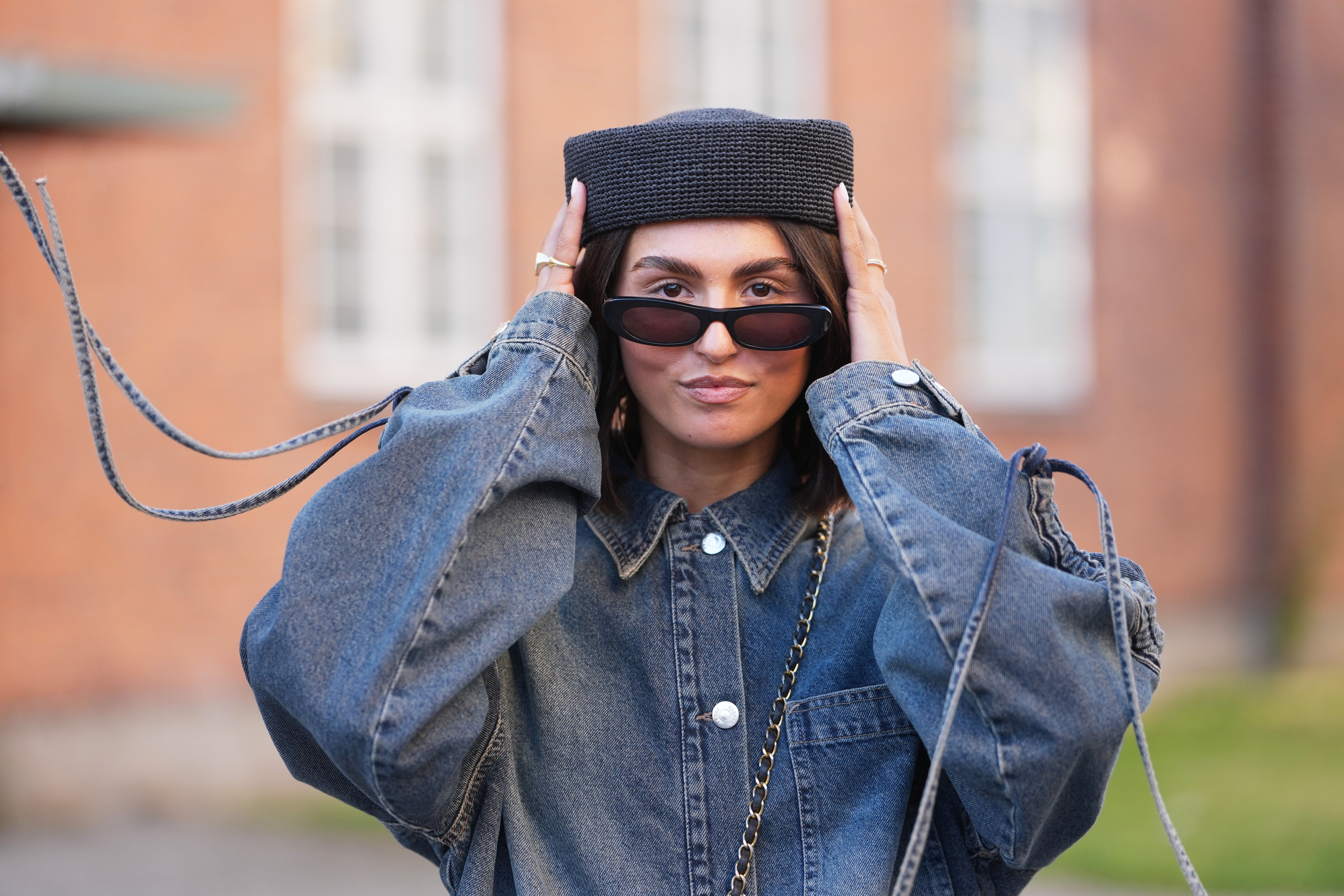 Frau mit schwarzem Barett, Sonnenbrille und übergroßer Jeansjacke mit Ballonärmeln.