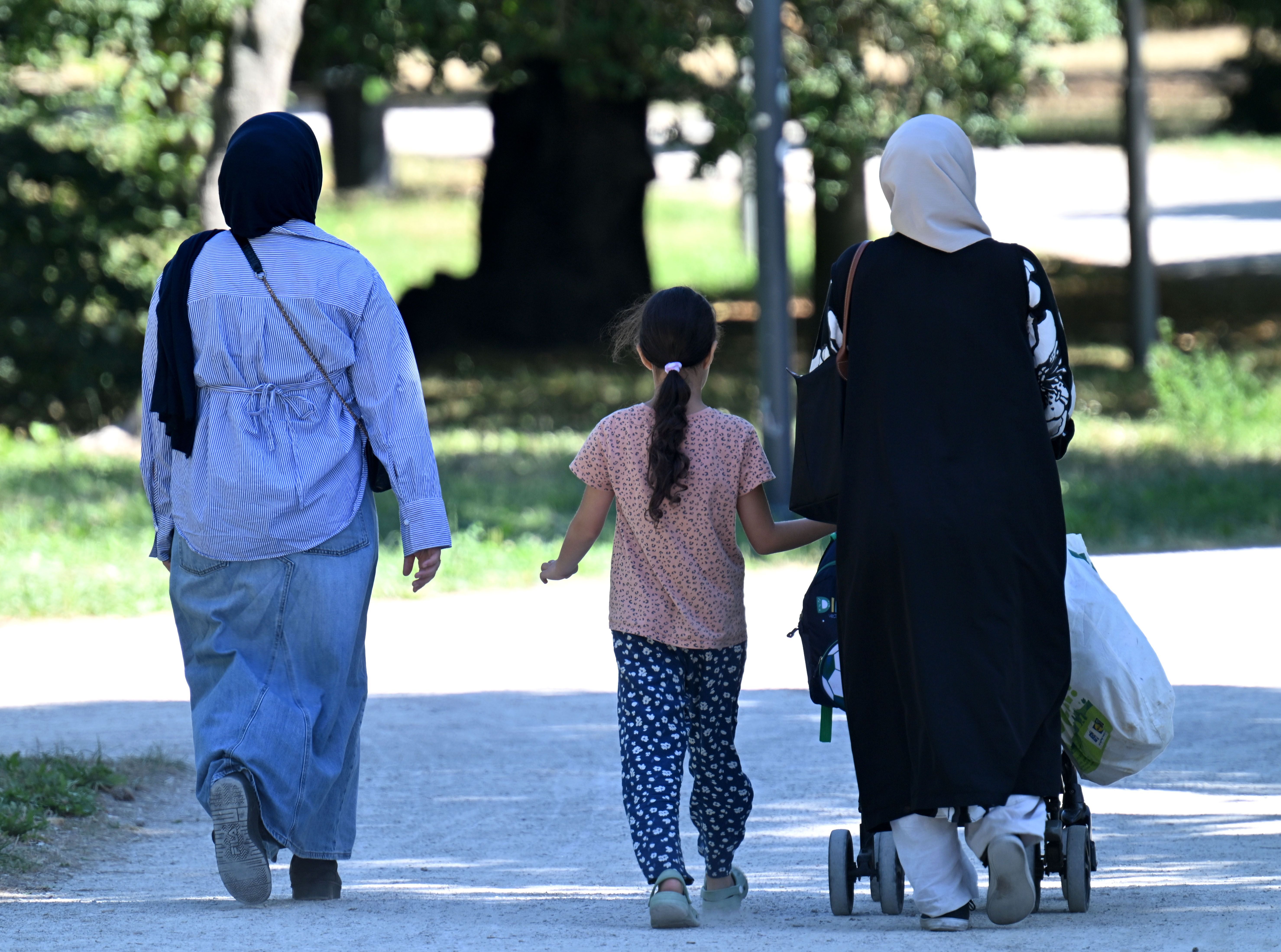 Zwei Frauen mit Kopftuch und ein Kind gehen mit Kinderwagen durch einen Park in Wien.