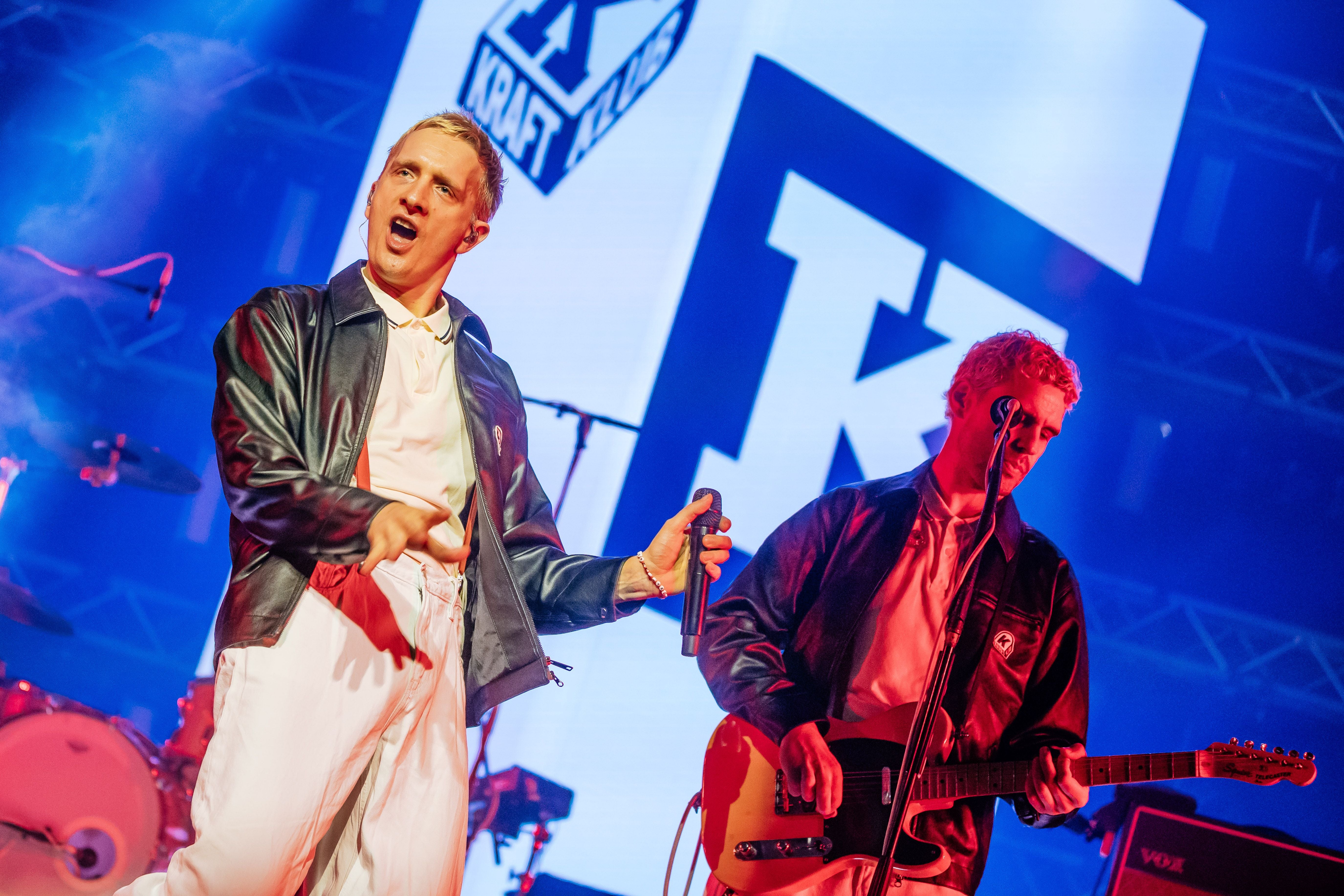 Zwei Musiker der Band Kraftklub performen auf einer Bühne mit großem K im Hintergrund.