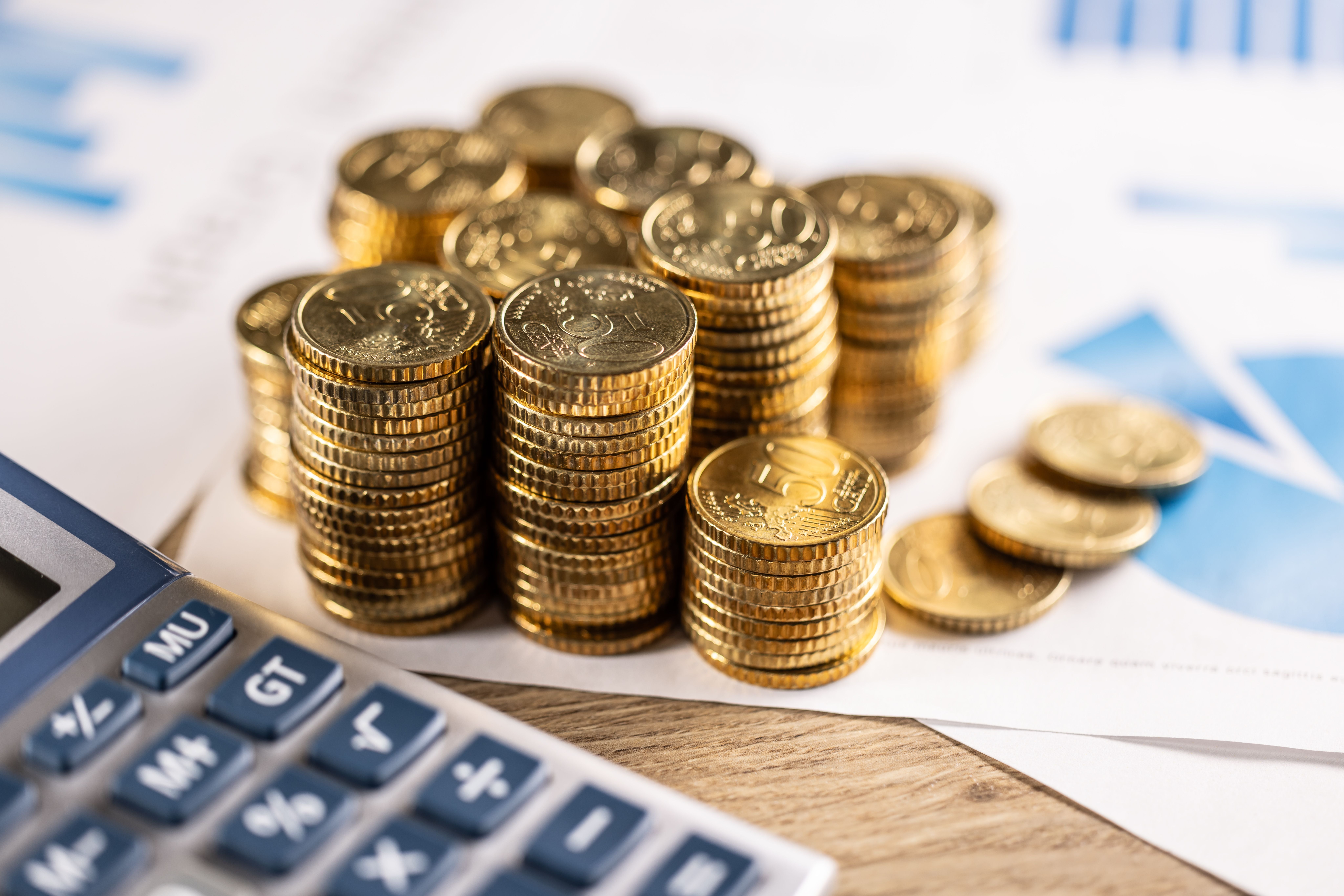 Gestapelte goldene 50-Cent-Euro-Münzen neben Taschenrechner und Finanzdiagrammen.