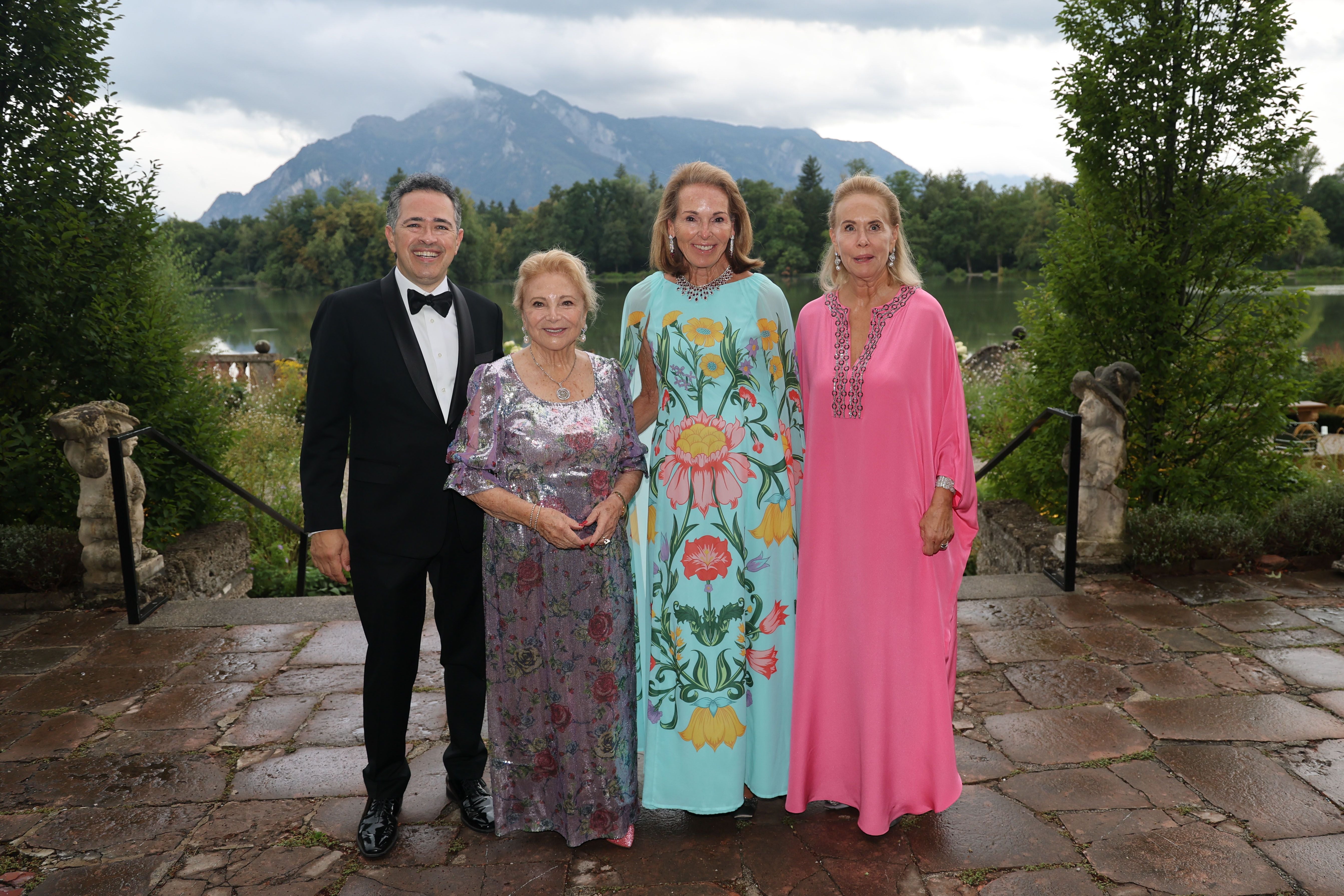 Vier elegant gekleidete Personen posieren vor See und Bergen im Garten von Schloss Leopoldskron.