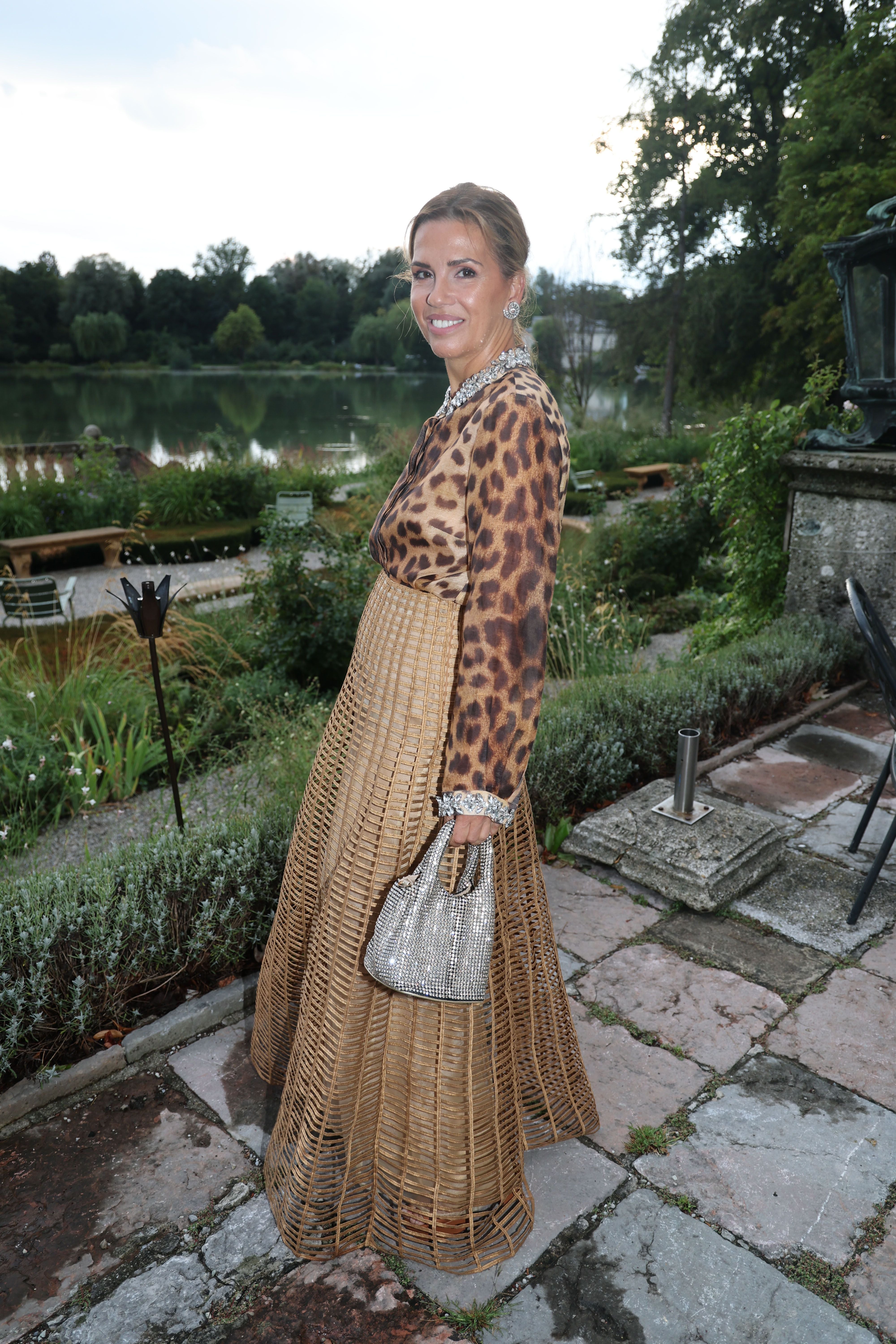 Frau in elegantem Abendkleid mit Leopardenmuster und Bastrock steht im Garten vor einem See.
