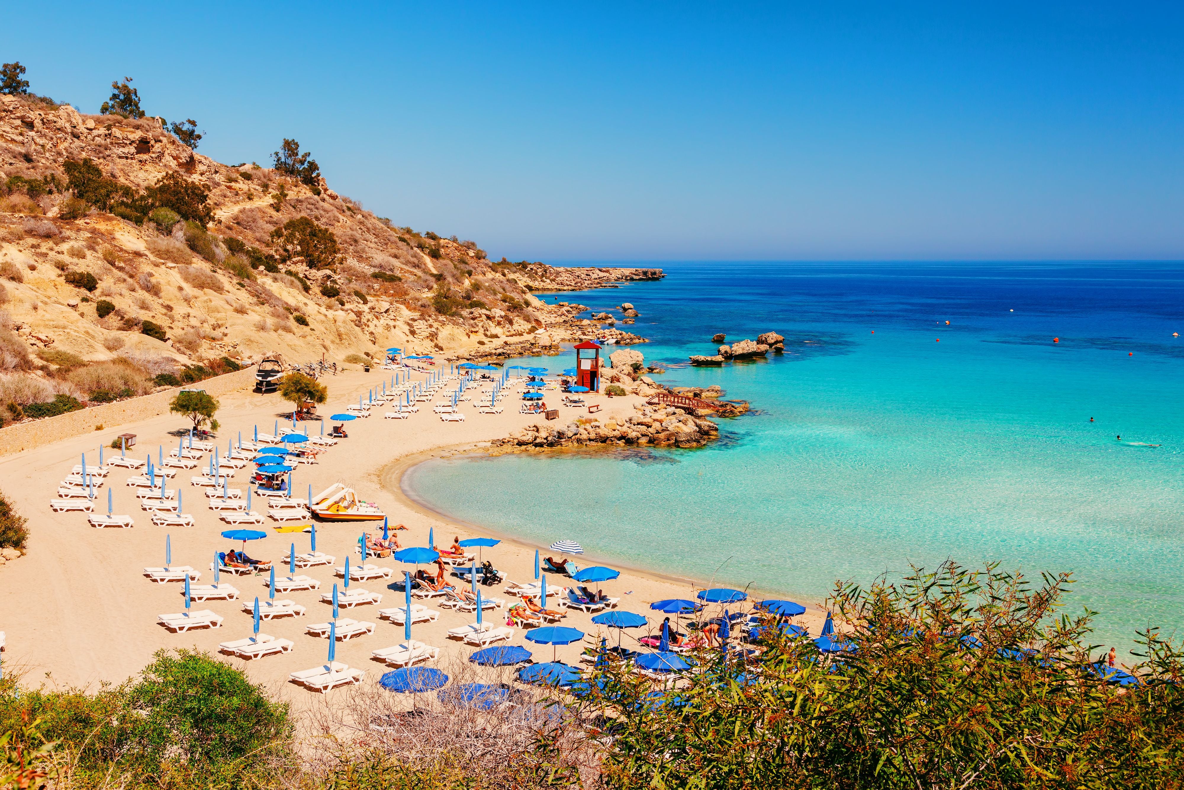 Feiner Sandstrand mit blauen Sonnenschirmen am türkisfarbenen Meer bei Ayia Napa, Zypern.