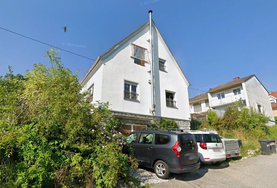 Weißes Wohnhaus mit geparkten Autos davor an einem sonnigen Tag.