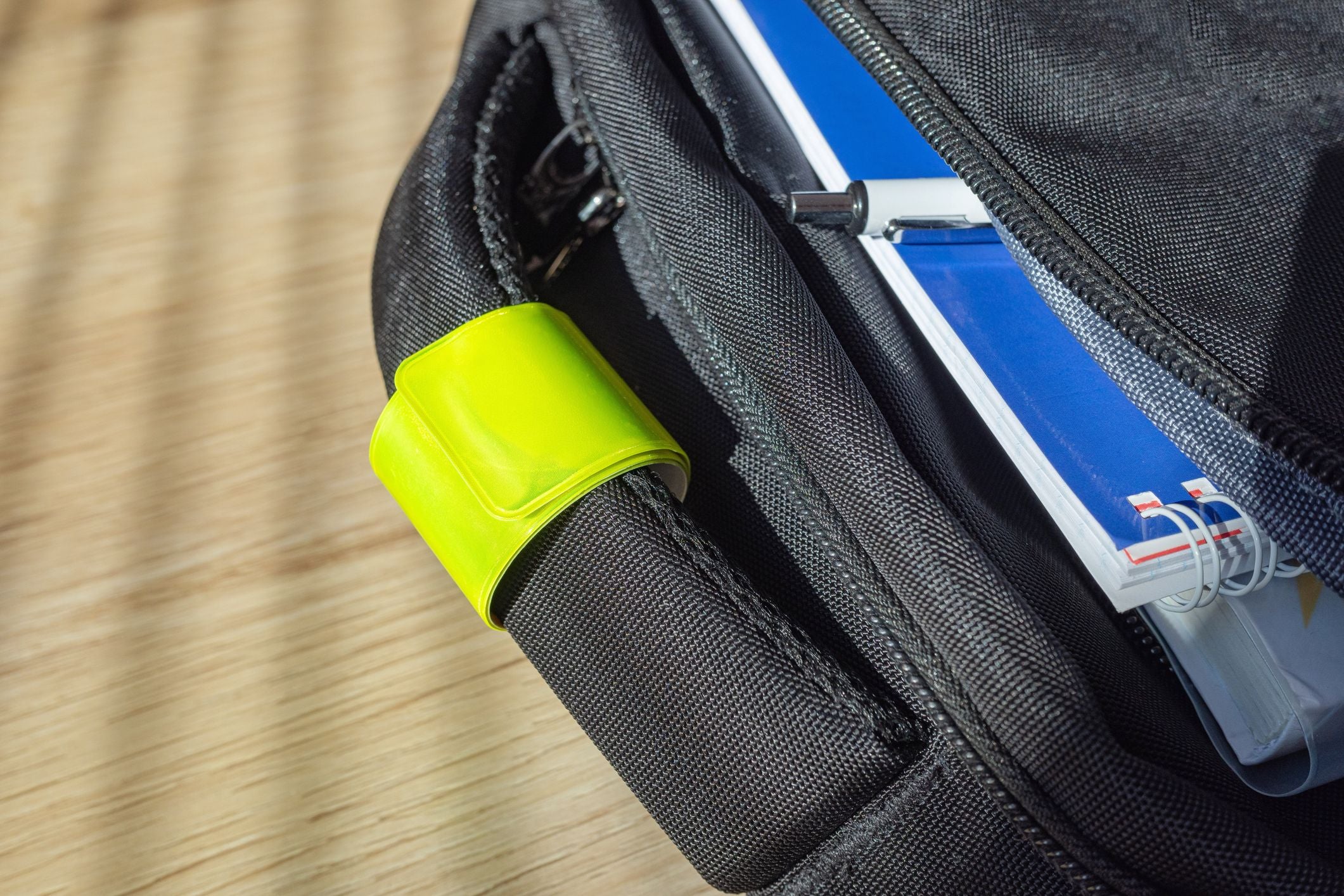 Gelbes reflektierendes Band an einem schwarzen Kinderrucksack mit Heften und Stift.