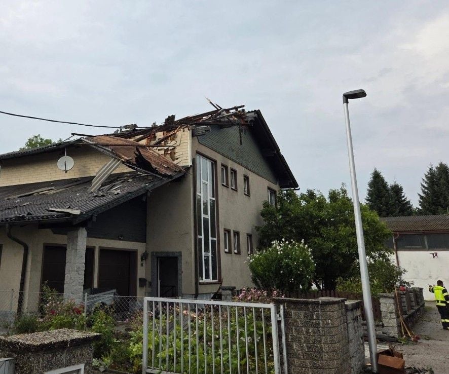 Haus mit stark beschädigtem Dach nach Tornado in Erferding, Feuerwehr am Einsatzort.