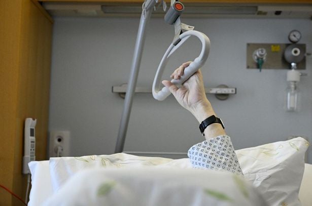 Eine Person liegt im Krankenhausbett und hält sich an einer Aufrichthilfe fest.