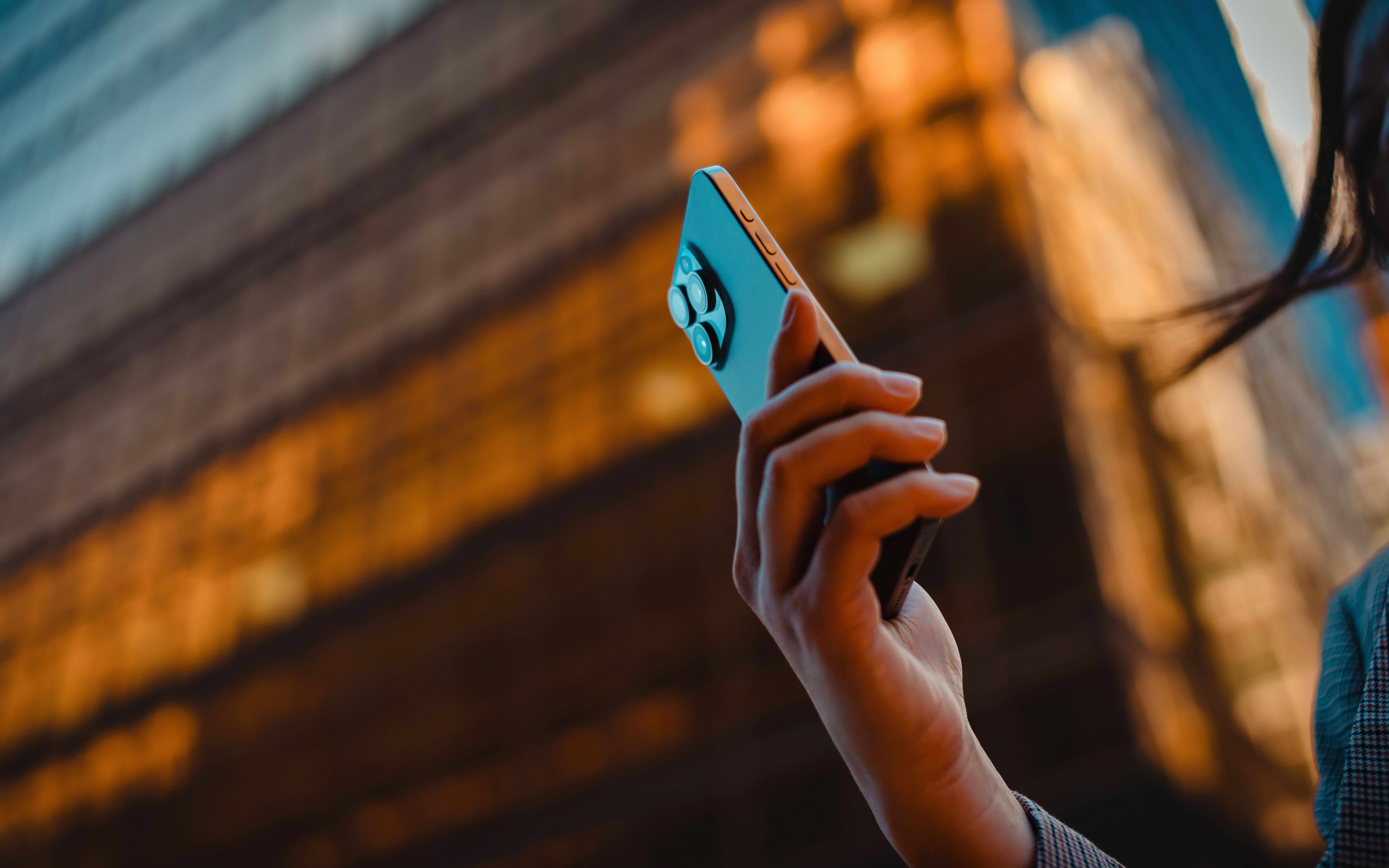 Frau hält Smartphone vor goldener Glasfassade eines modernen Bürogebäudes in der Stadt.