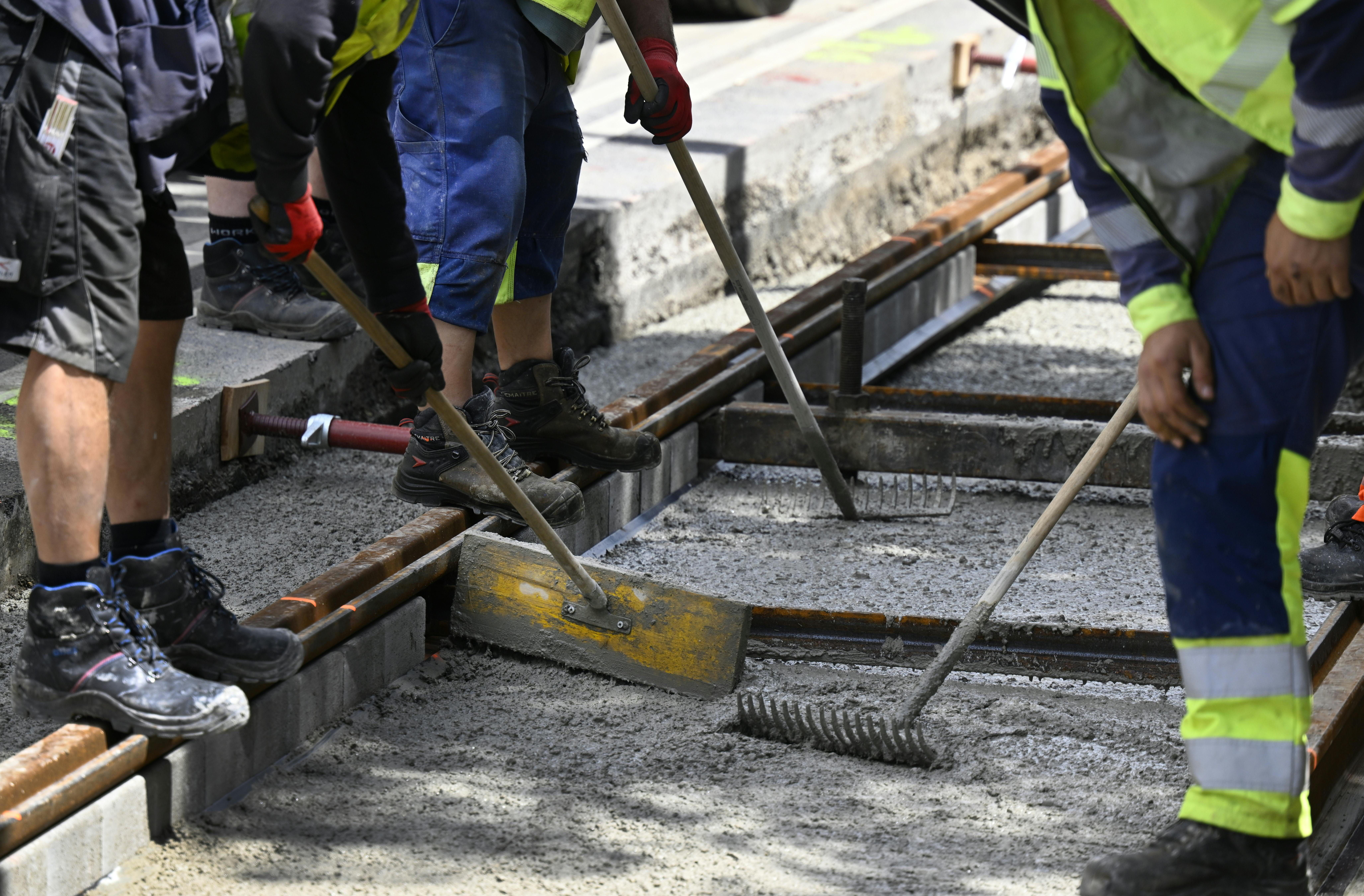 Bauarbeiter arbeiten auf einer Straßenbahn-Gleisbaustelle und verteilen frischen Beton.