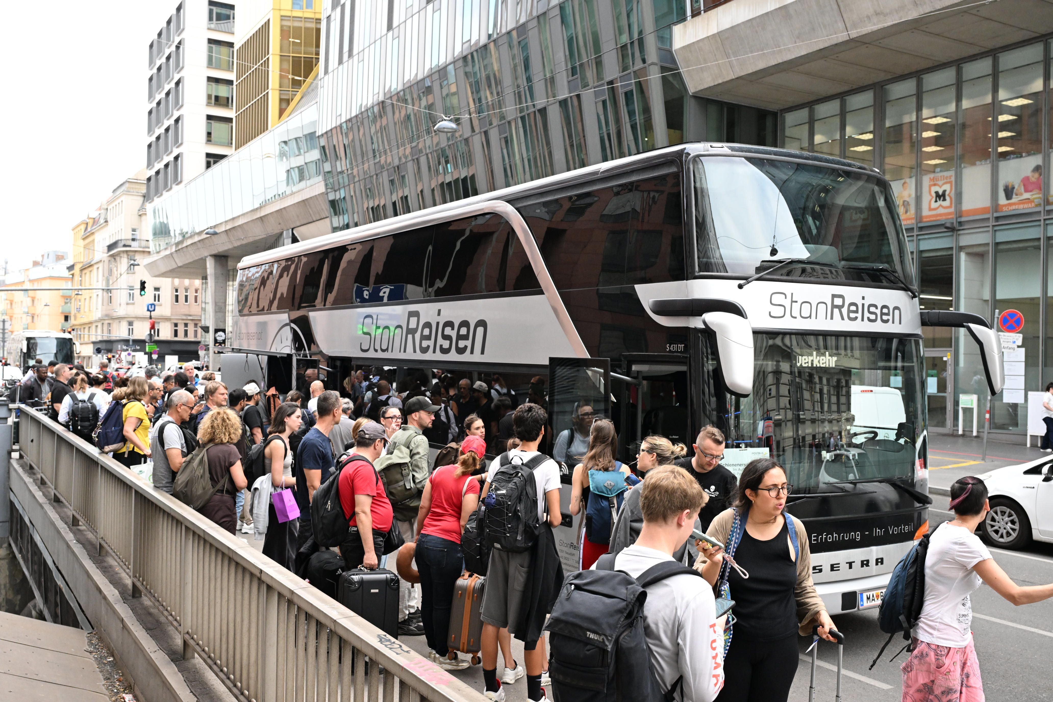 Viele Menschen mit Gepäck steigen an einer Straßenecke in einen Reisebus der Firma StanReisen ein.