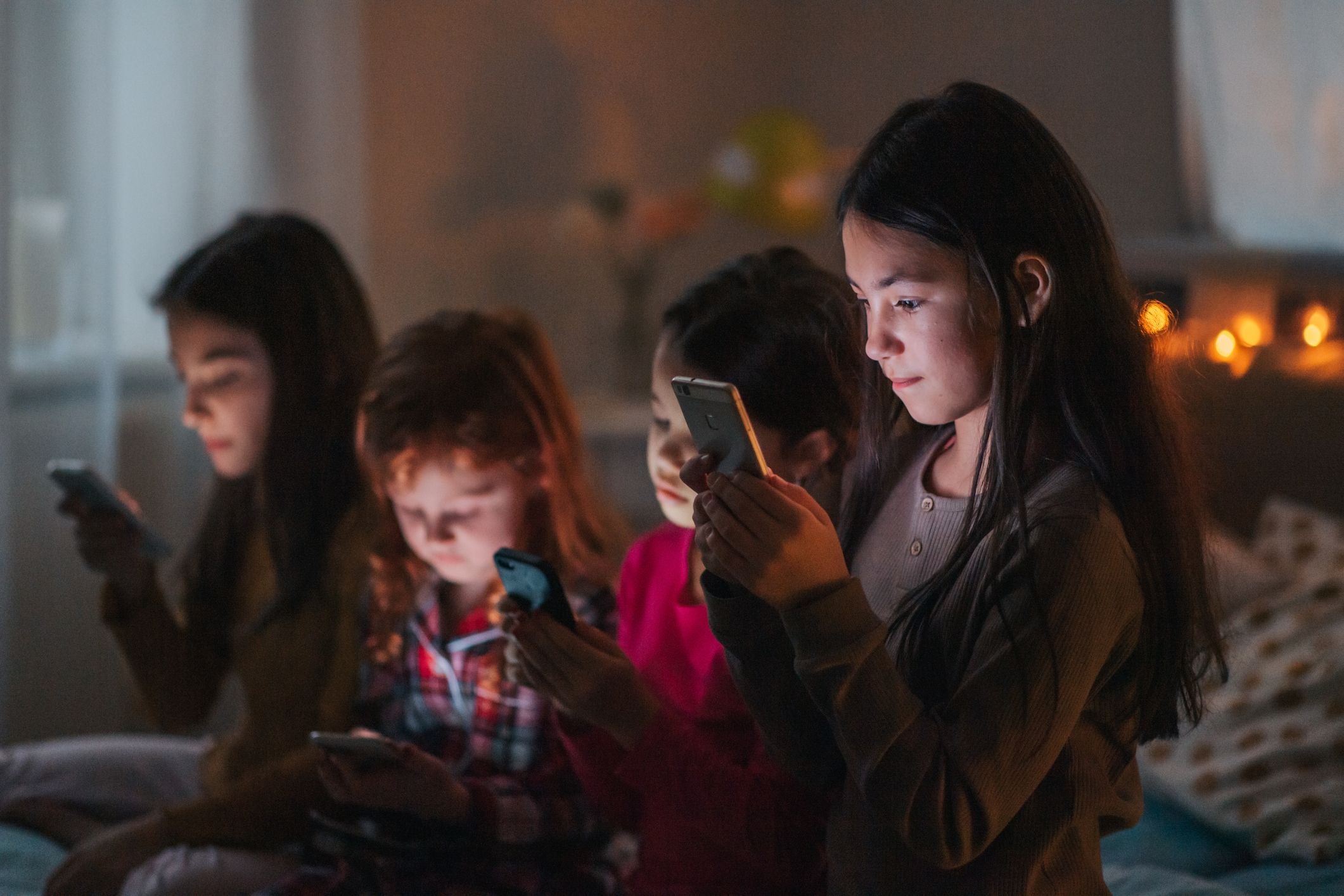 Vier Mädchen schauen bei einer Pyjamaparty gemeinsam auf ihre Smartphones.