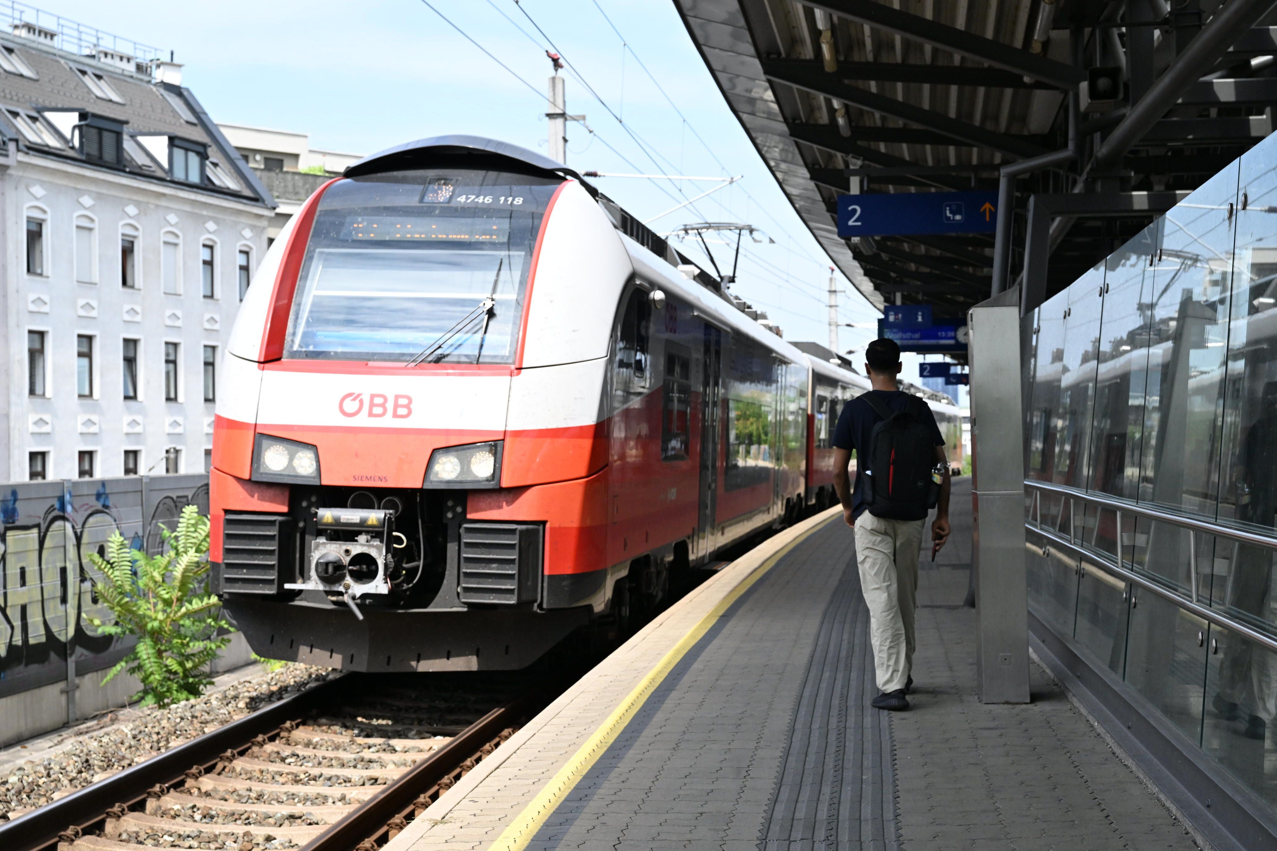 Ein ÖBB-Zug fährt in einen Bahnhof ein, ein Mann mit Rucksack steht am Bahnsteig.